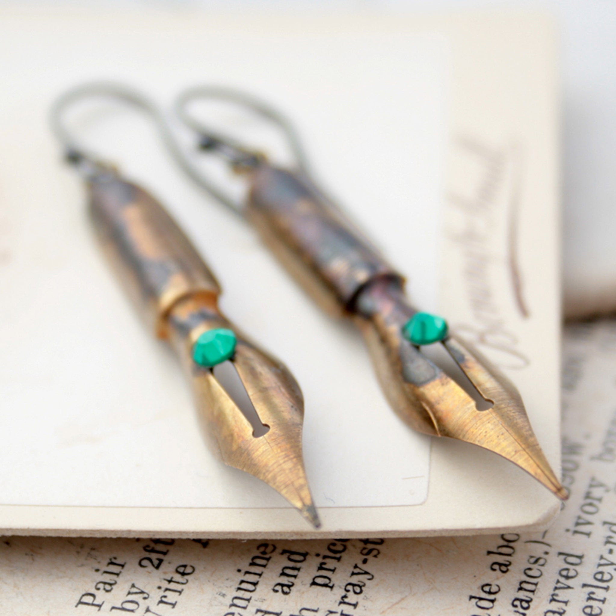 gold earrings made of real pen nibs with turquoise crystals lying on an old photograph