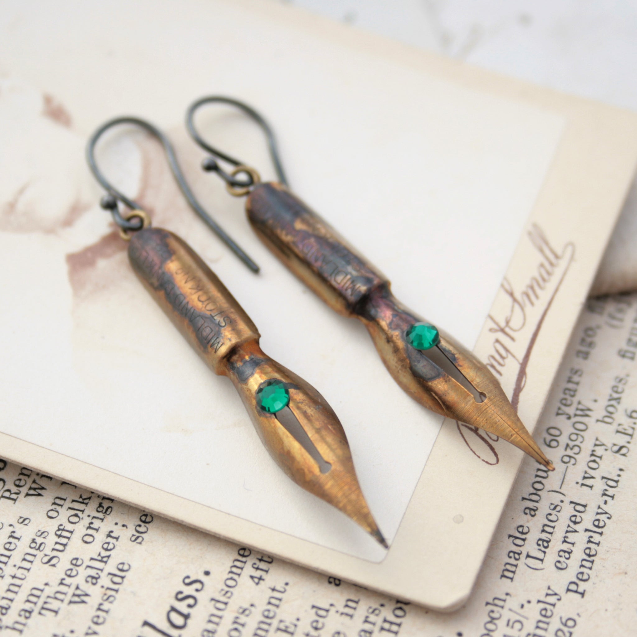 gold earrings made of real pen nibs with turquoise crystals lying on an old photograph