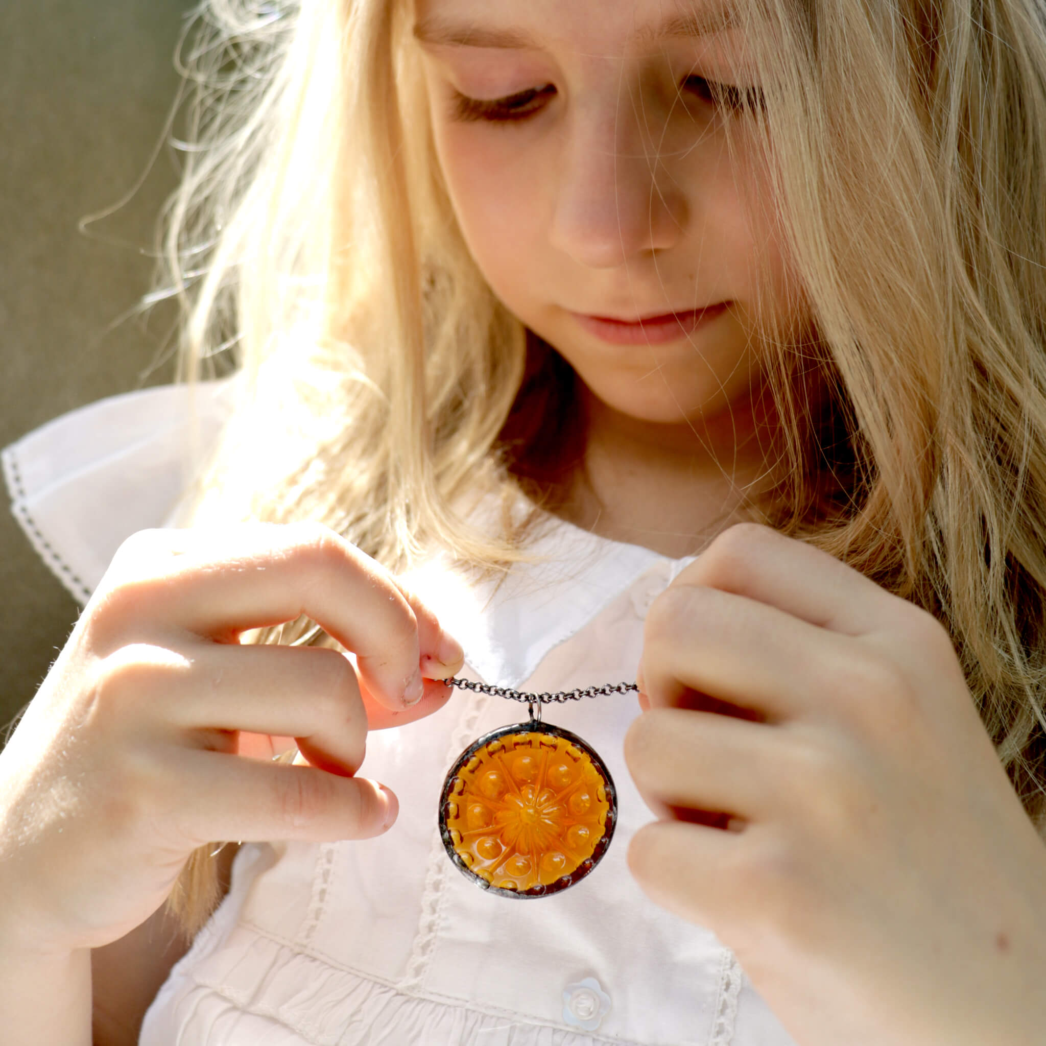 Blonde girl in white dress holding amber necklace in hands