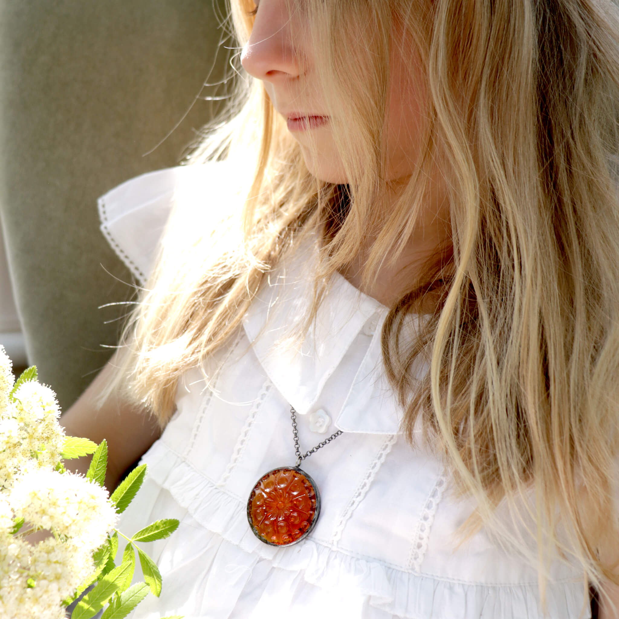 Blonde girl in white dress wearing amber necklace holding bunch of flowers