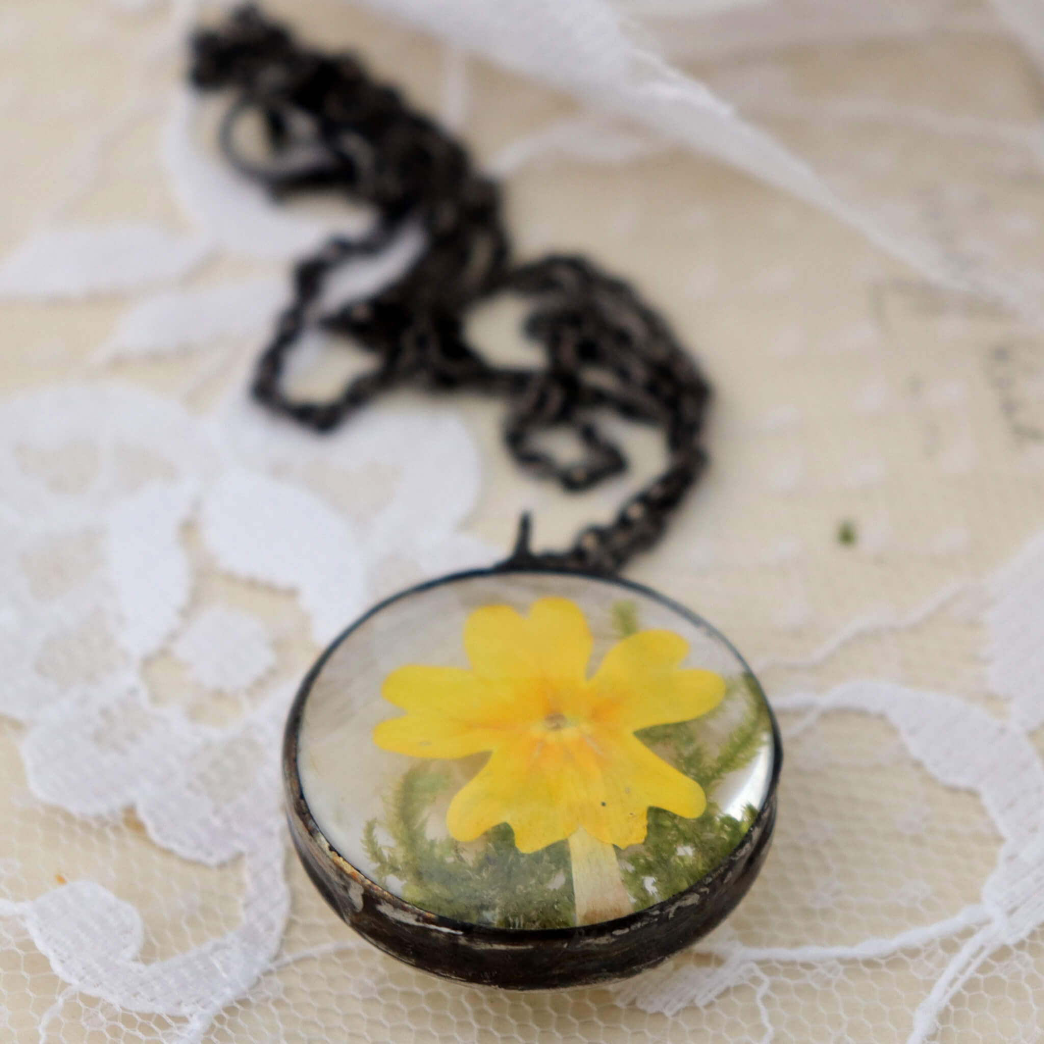 Primroses in soldered glass necklace on a lacy background