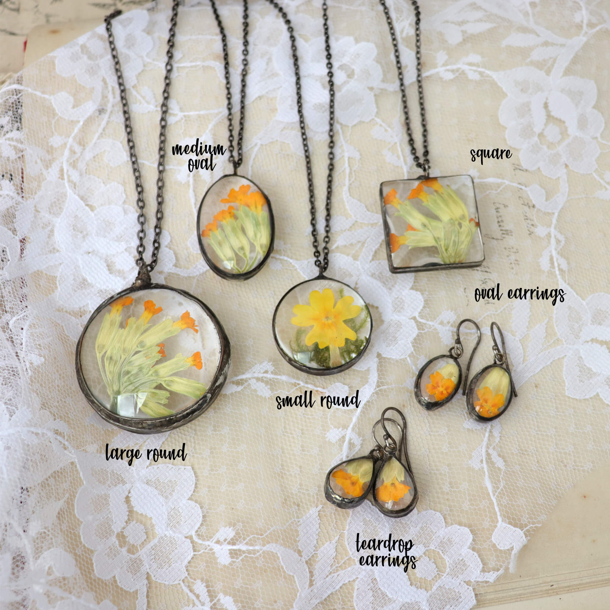 Primrose flowers in soldered glass jewellery selection lying on a white lace