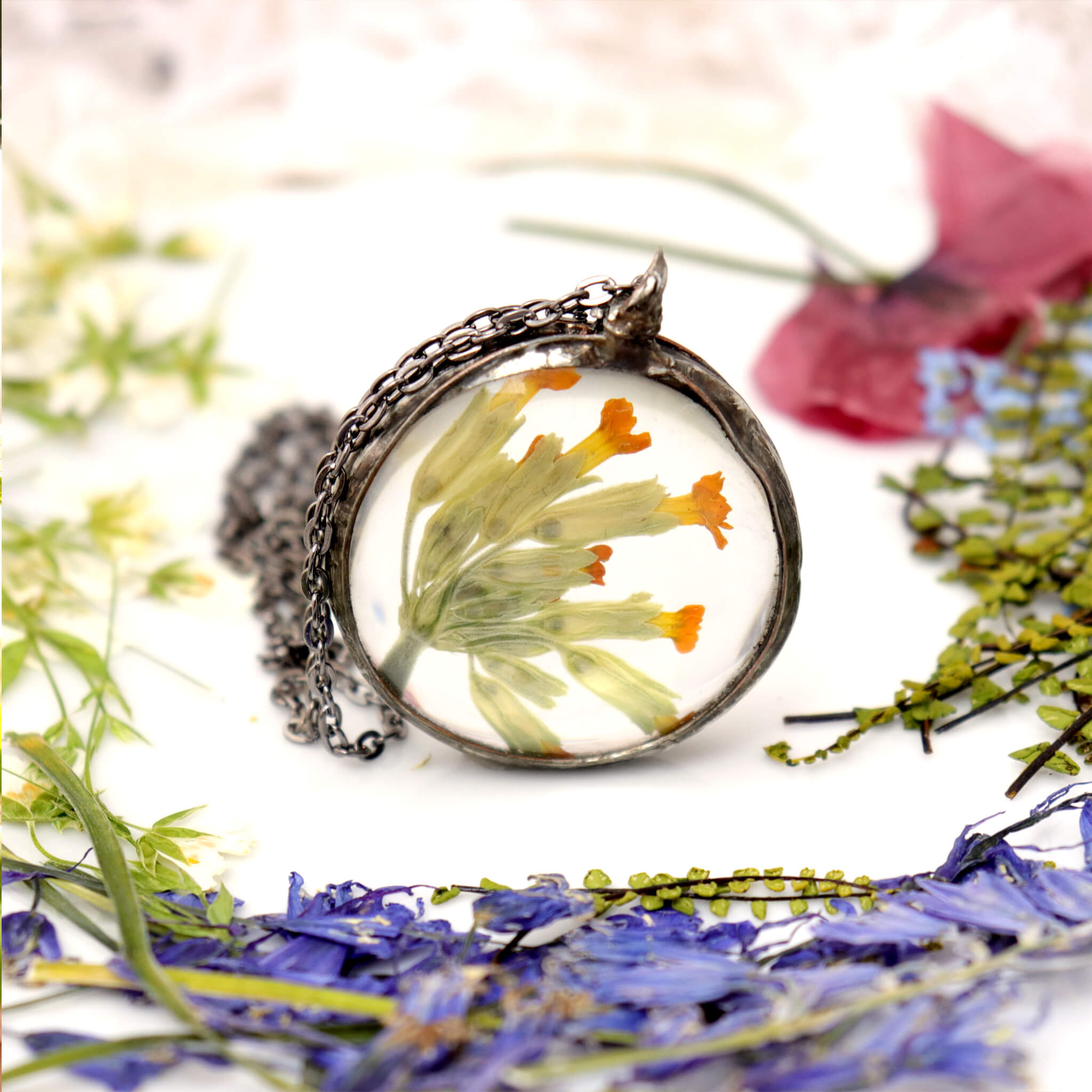 Primroses in soldered glass necklace on a white background, different pressed flowers around