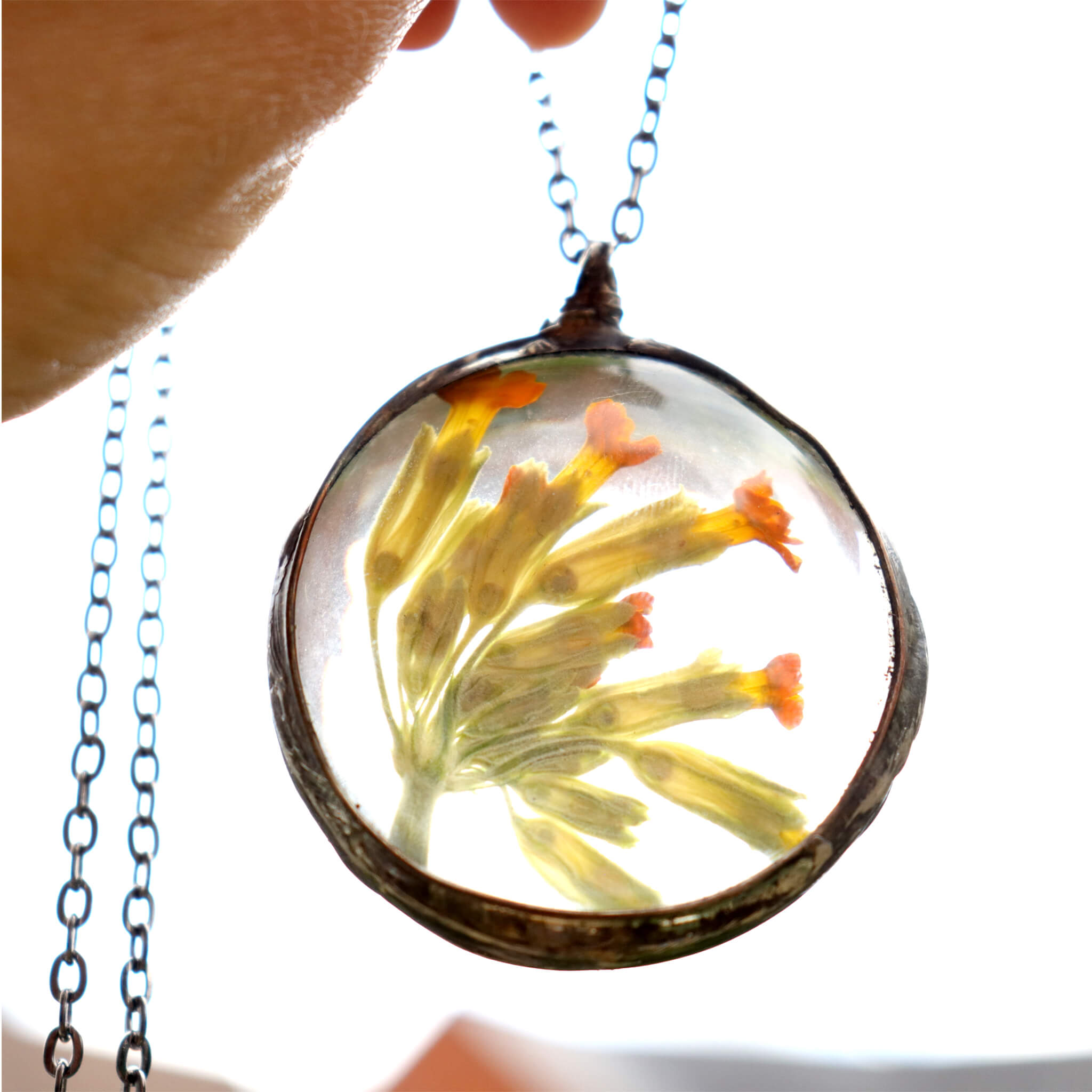 Primroses in soldered glass necklace on a white background