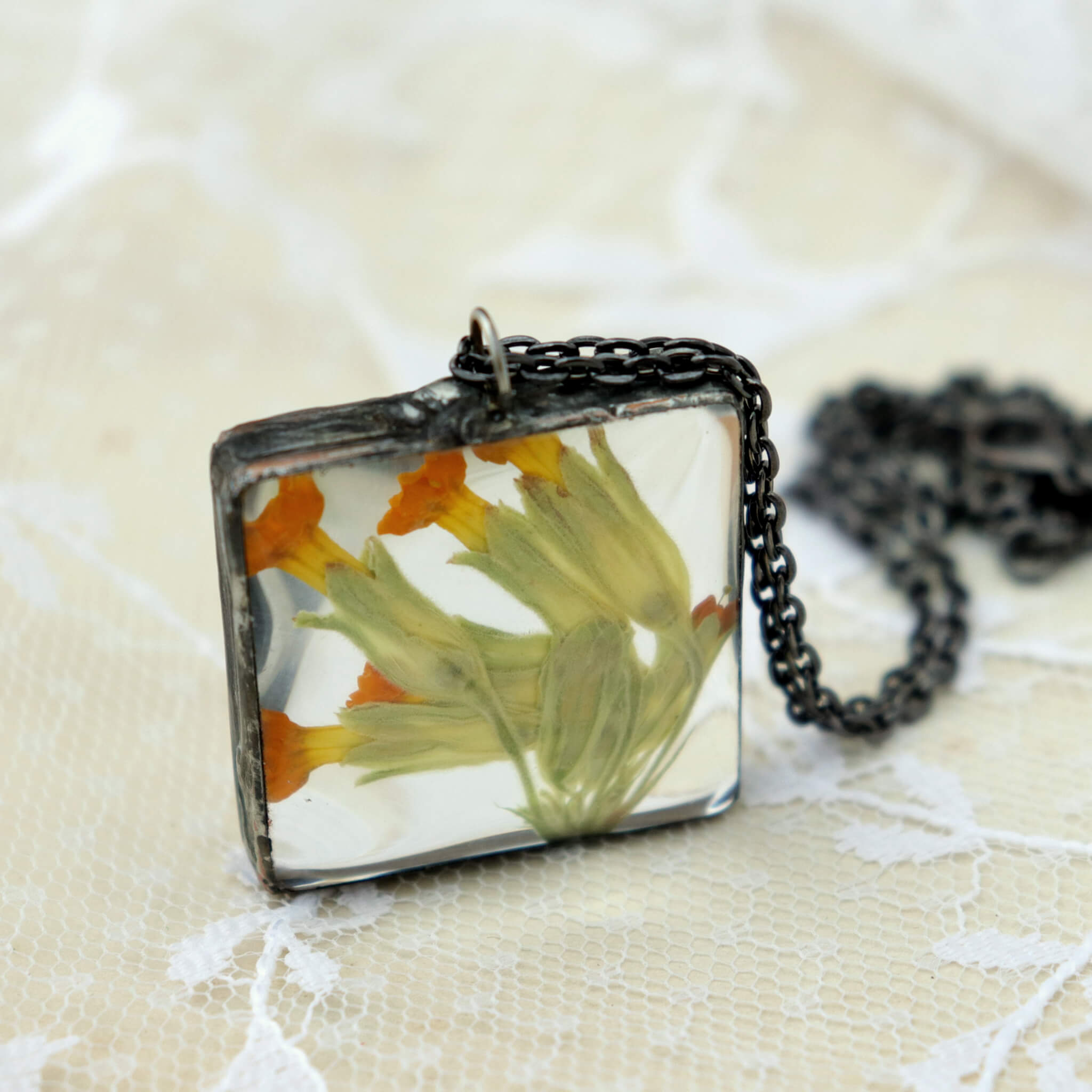 Primroses in soldered square glass necklace on a lacy background