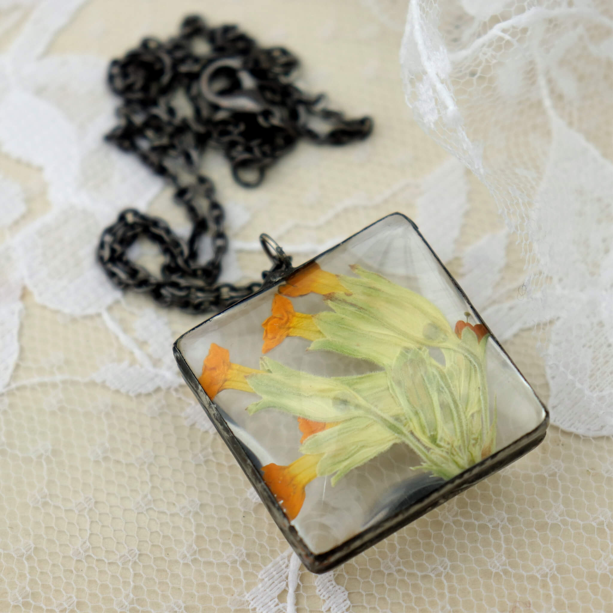 Primroses in soldered square glass necklace on a lacy background