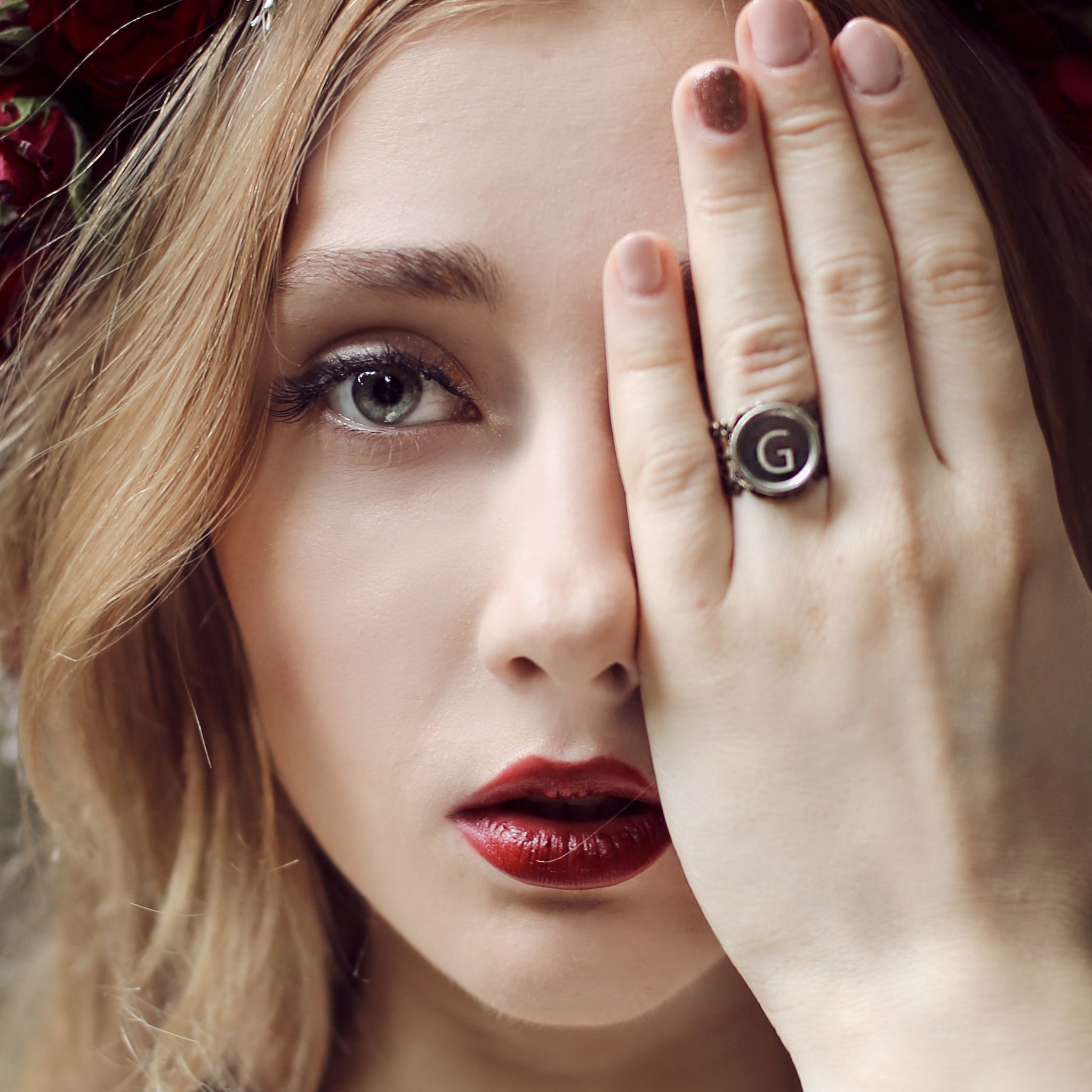 Woman covering her eye with a hand wearing initial ring made of typewriter key