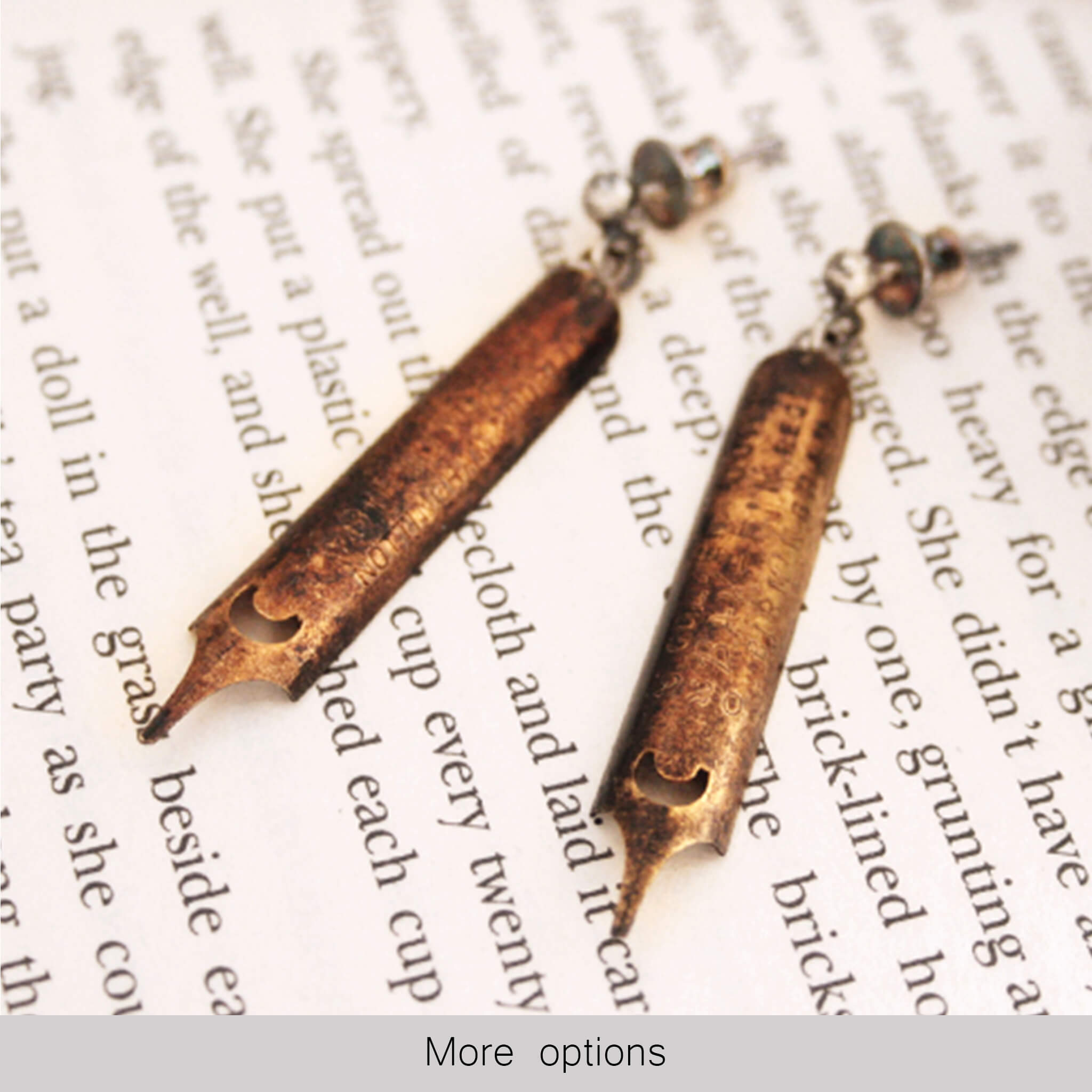 antique gold pen nib earrings covered in patina lying on a page of text