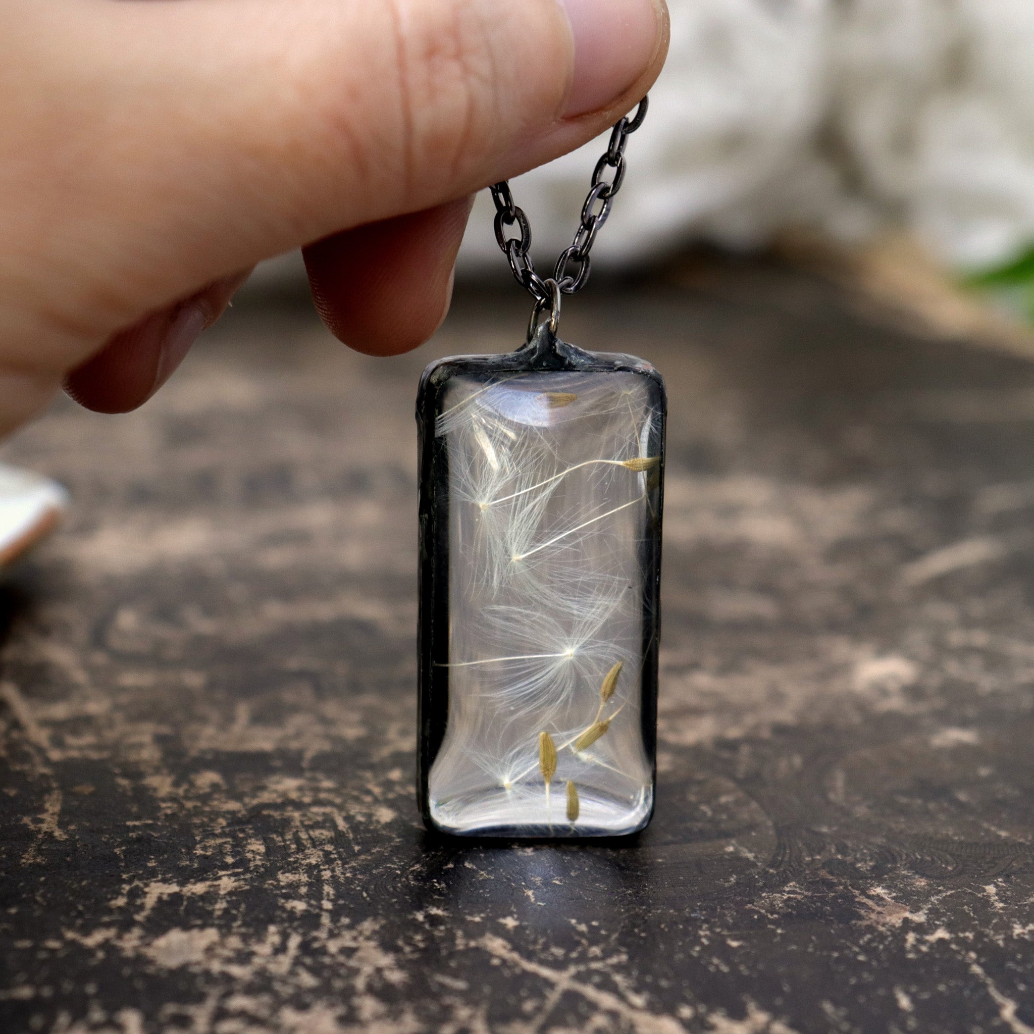 Dandelion seeds in a glass, rectangular necklace on a brown background