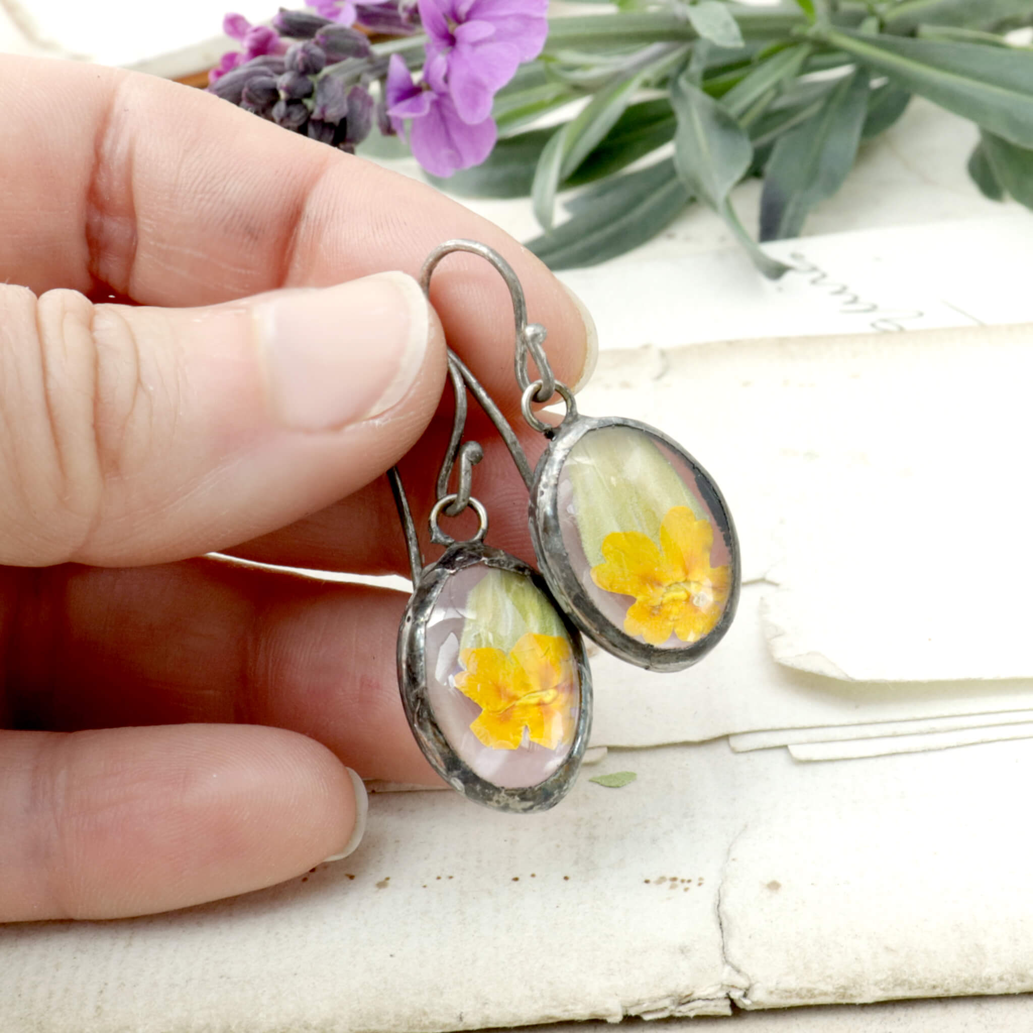 Hand holding primroses in soldered glass earrings by an old letter