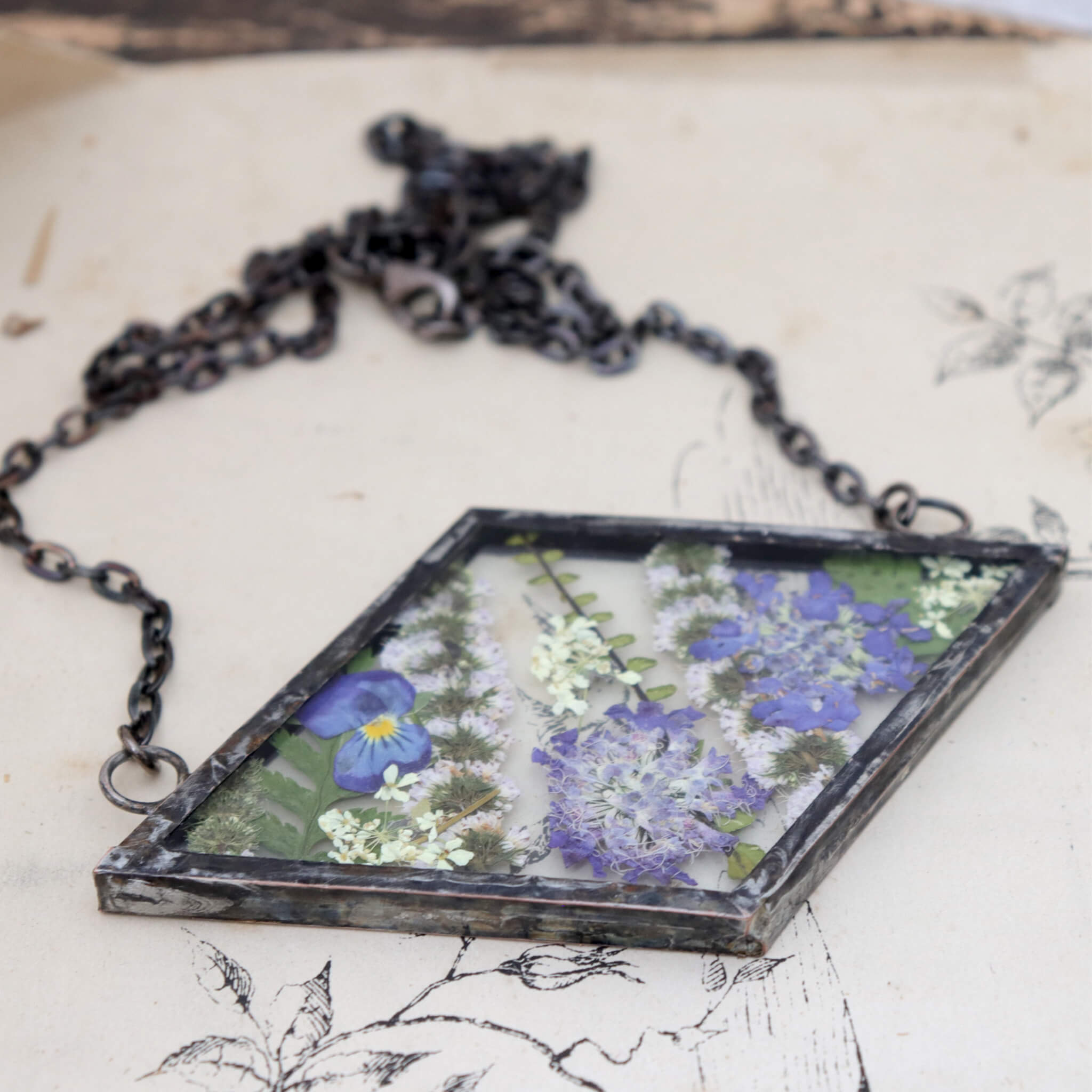 Rhomboidal purple pressed flower necklace lying on an old book