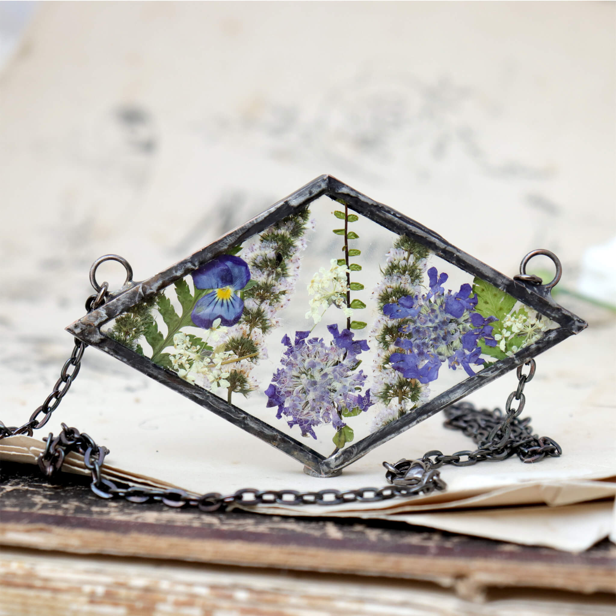 Rhomboidal purple pressed flower necklace standing on an old book