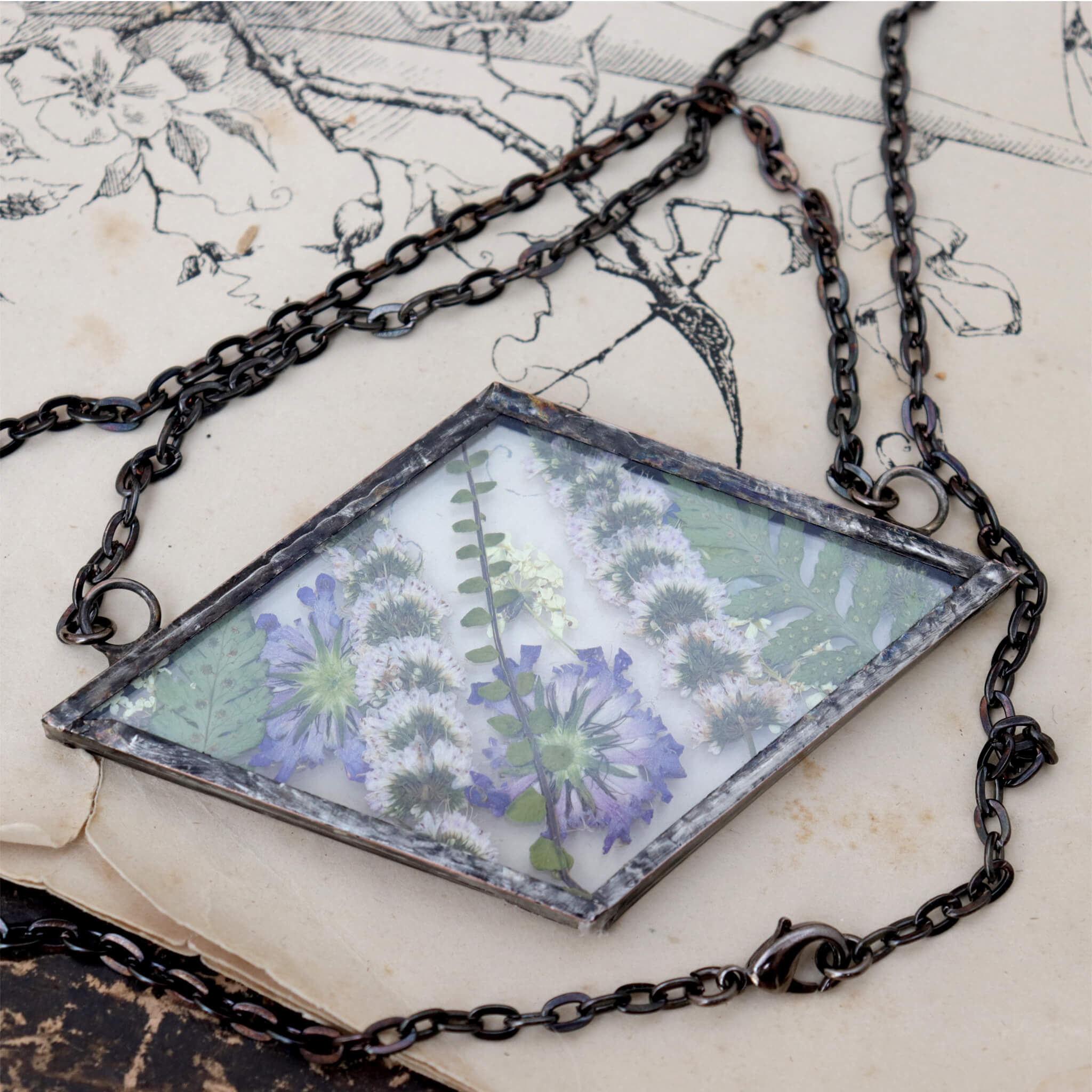 Rhomboidal purple pressed flower necklace lying on an old book