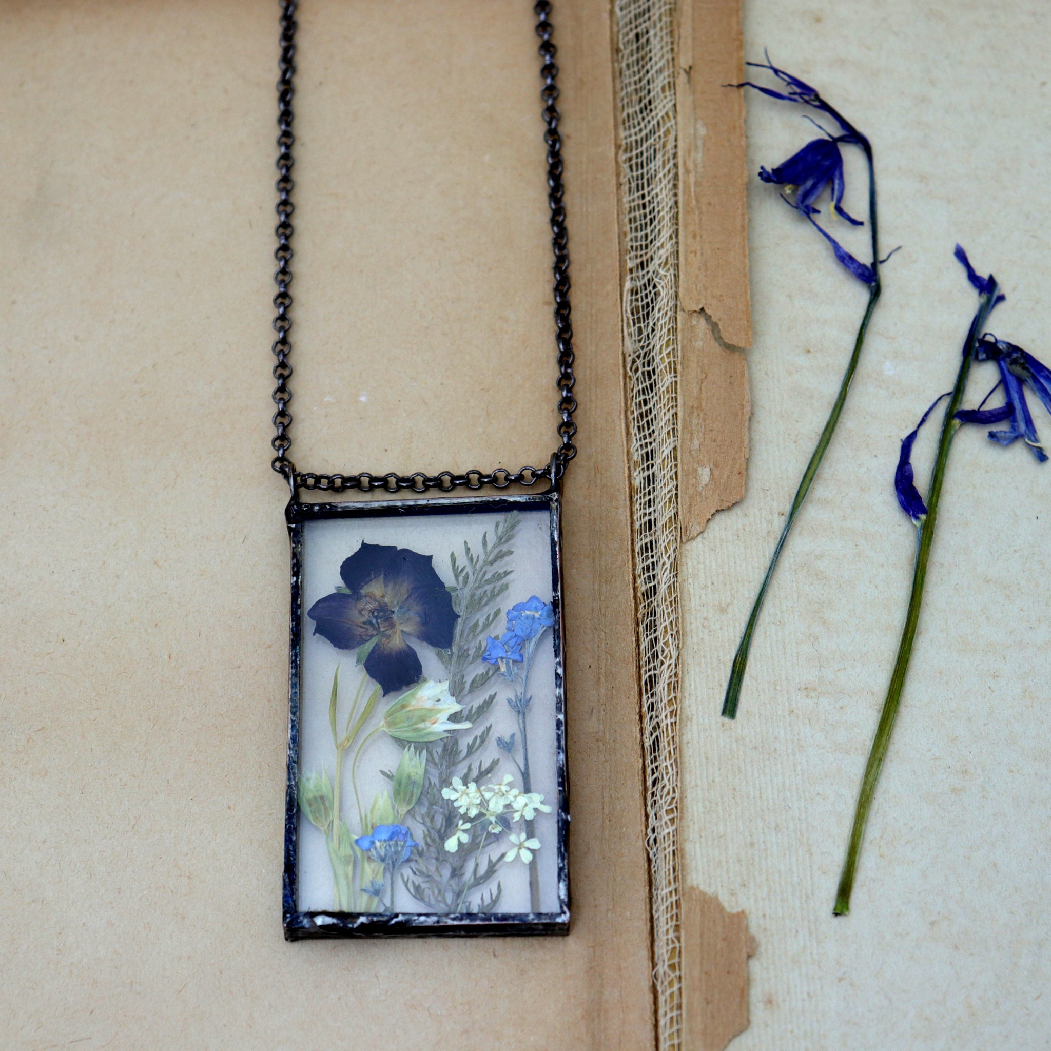 Pressed Meadow flower necklace lying on an old book by some preddes bluebells