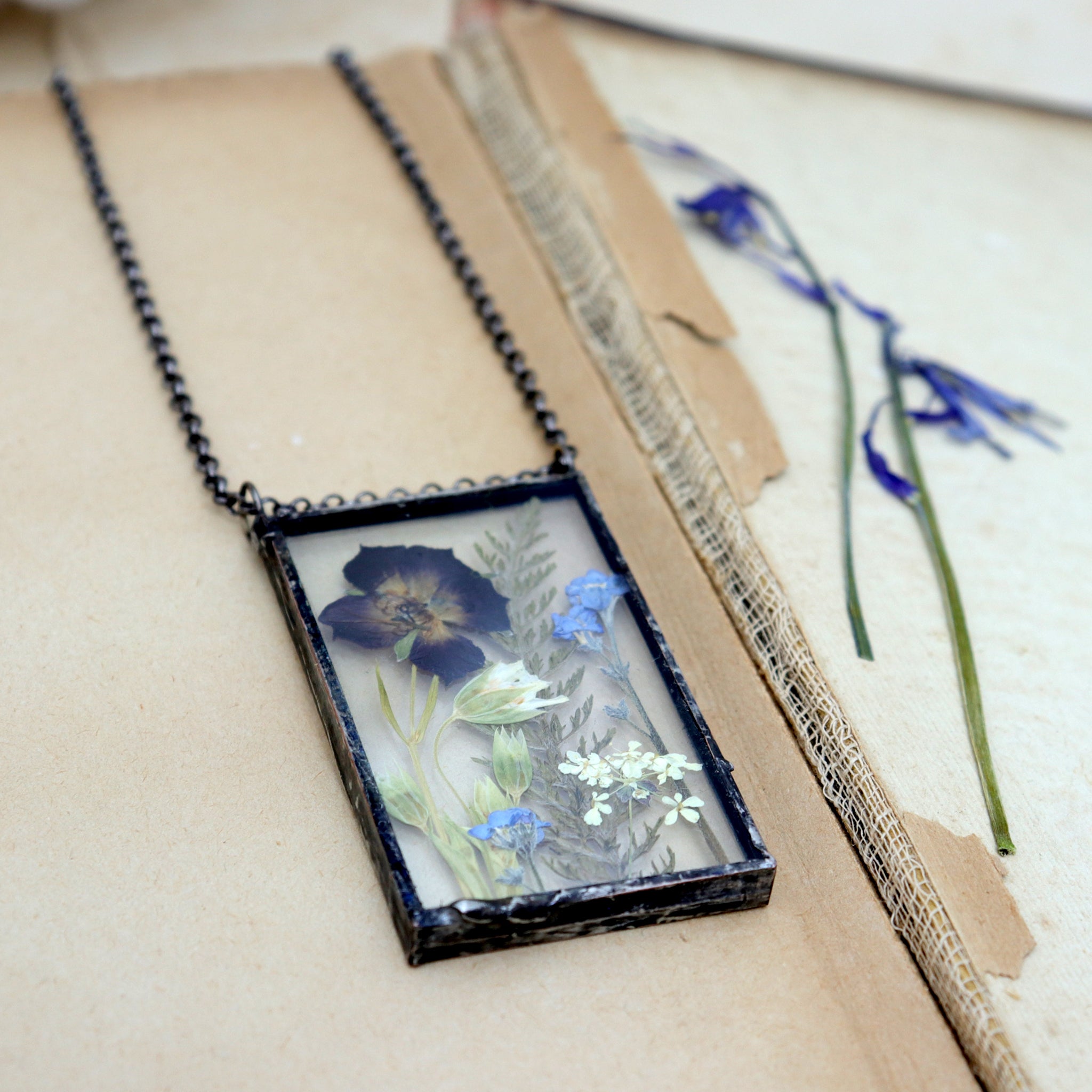 Pressed Meadow flower necklace lying on an old book by some preddes bluebells