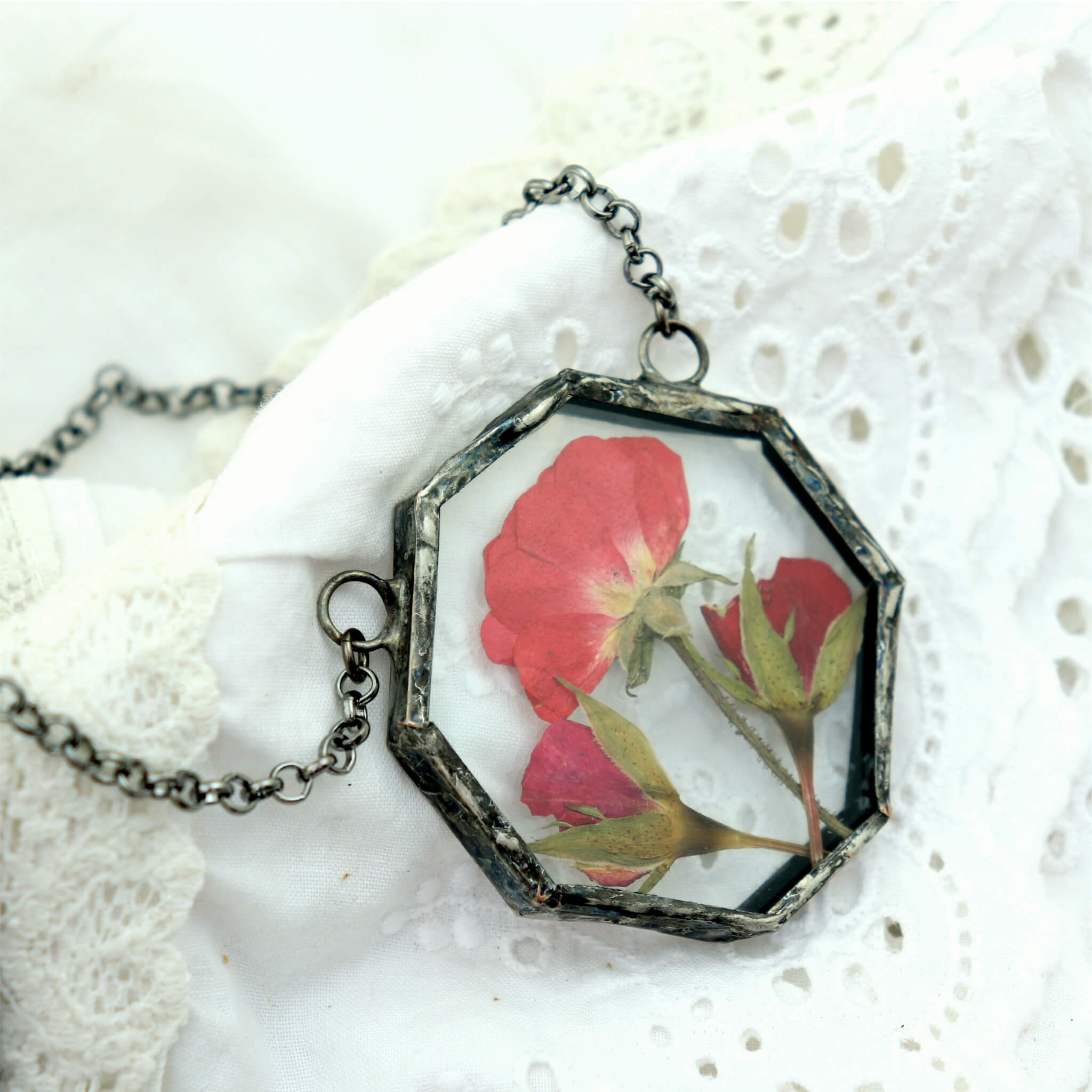Pressed rose in soldered hexagon glass pendant necklace lying on white lace