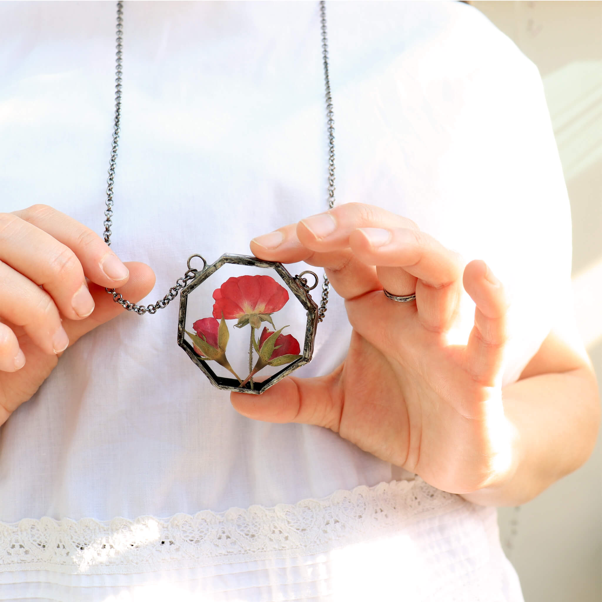 Hands playing with pressed rose pendant necklace