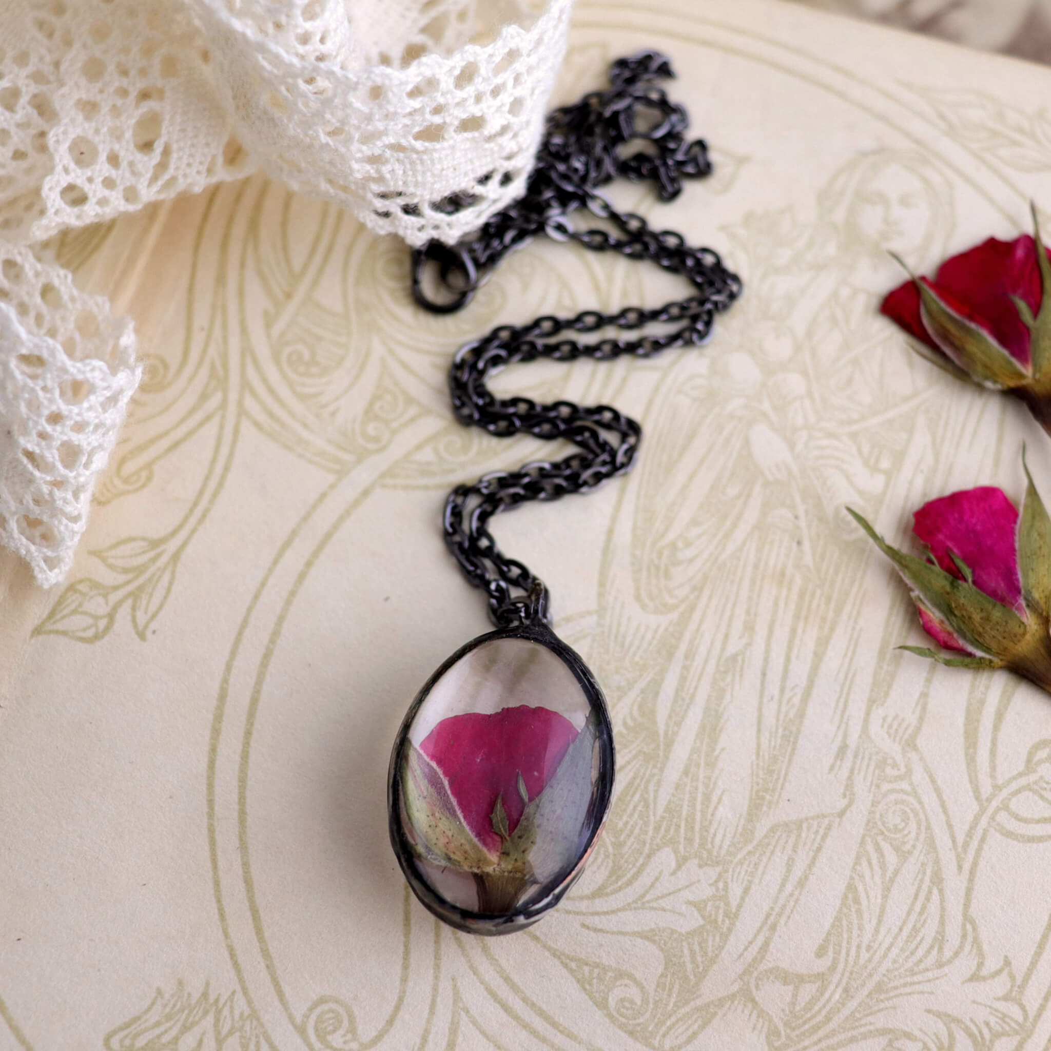 Pressed rose in soldered glass pendant necklace lying on an old book