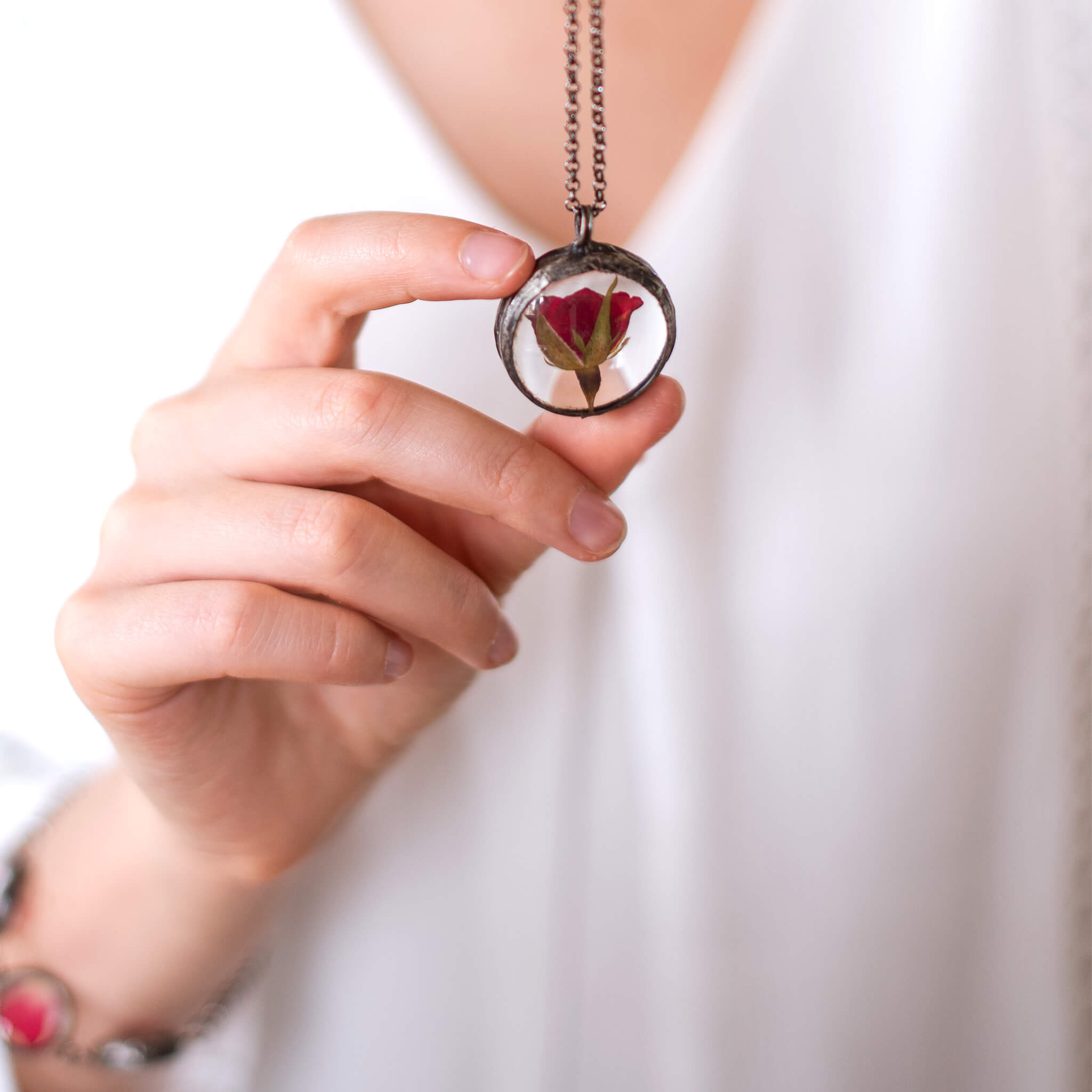 Hand holding pressed rose pendant necklace