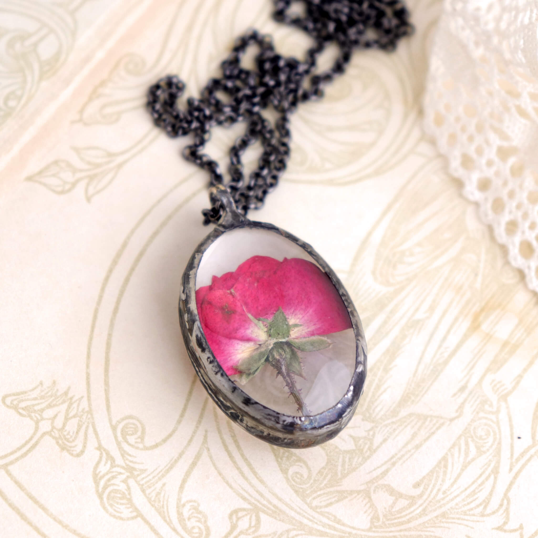 Pressed rose in soldered glass pendant necklace lying on an old book