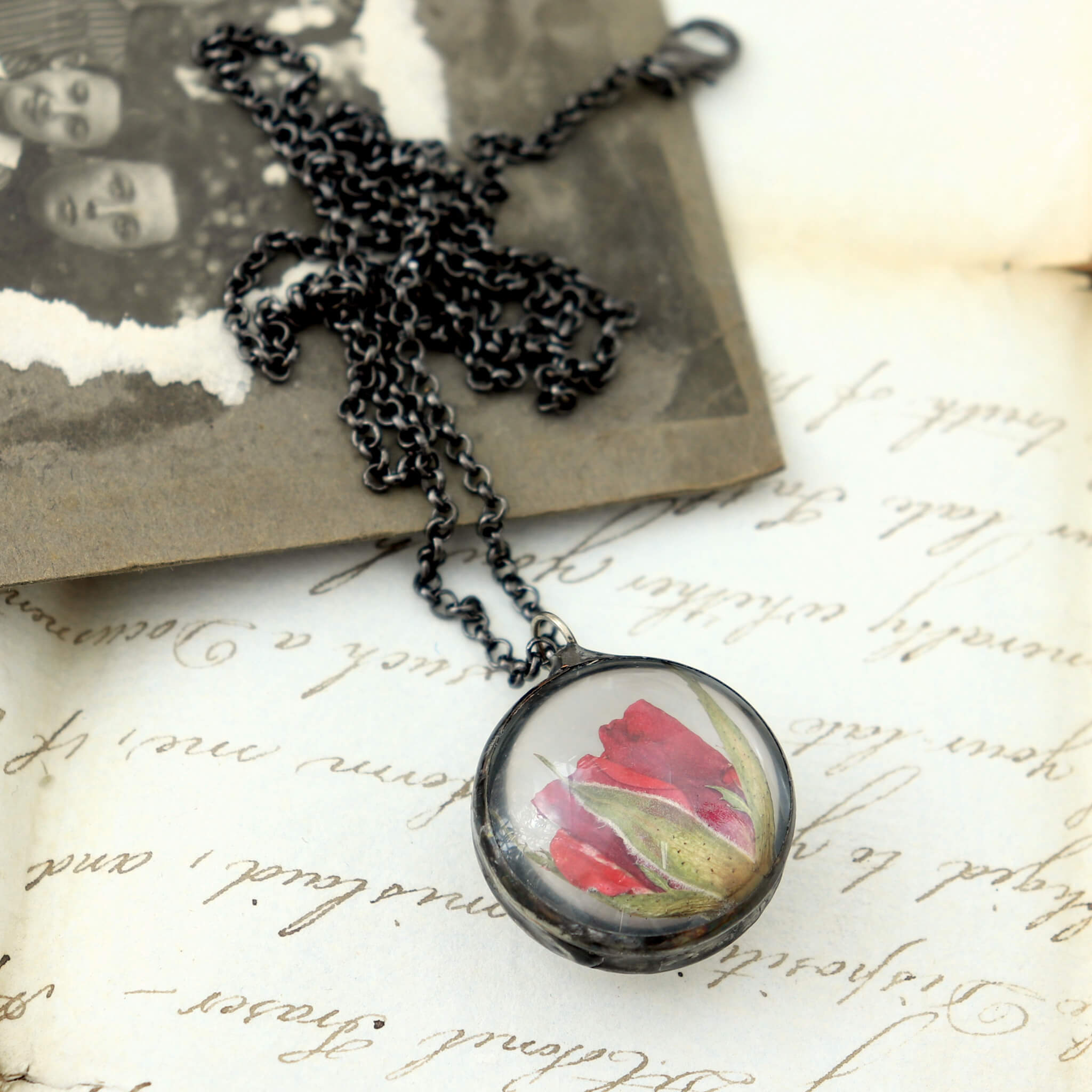 pressed rose pendant necklace lying on an old letter and photo