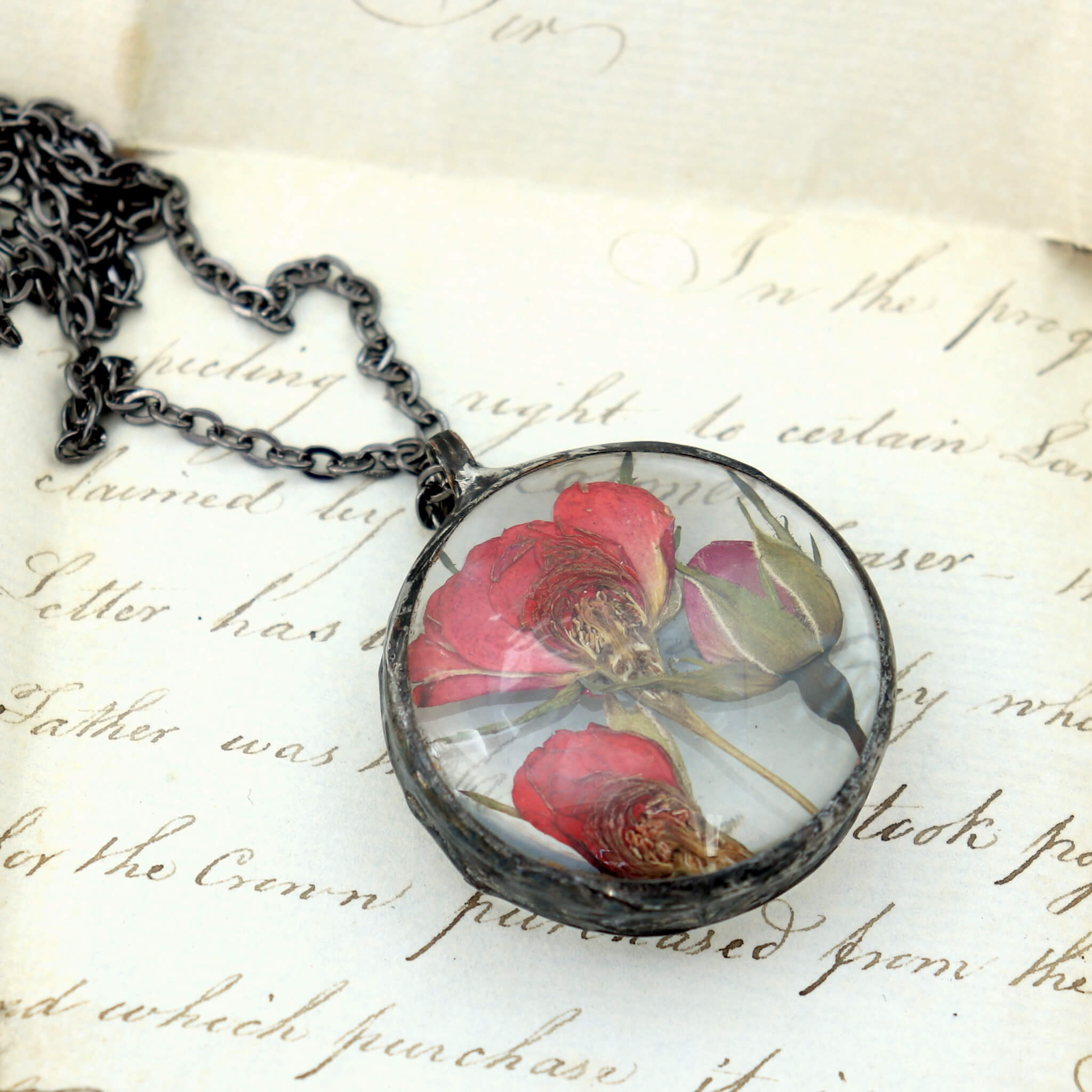 pressed rose pendant necklace lying on an old letter