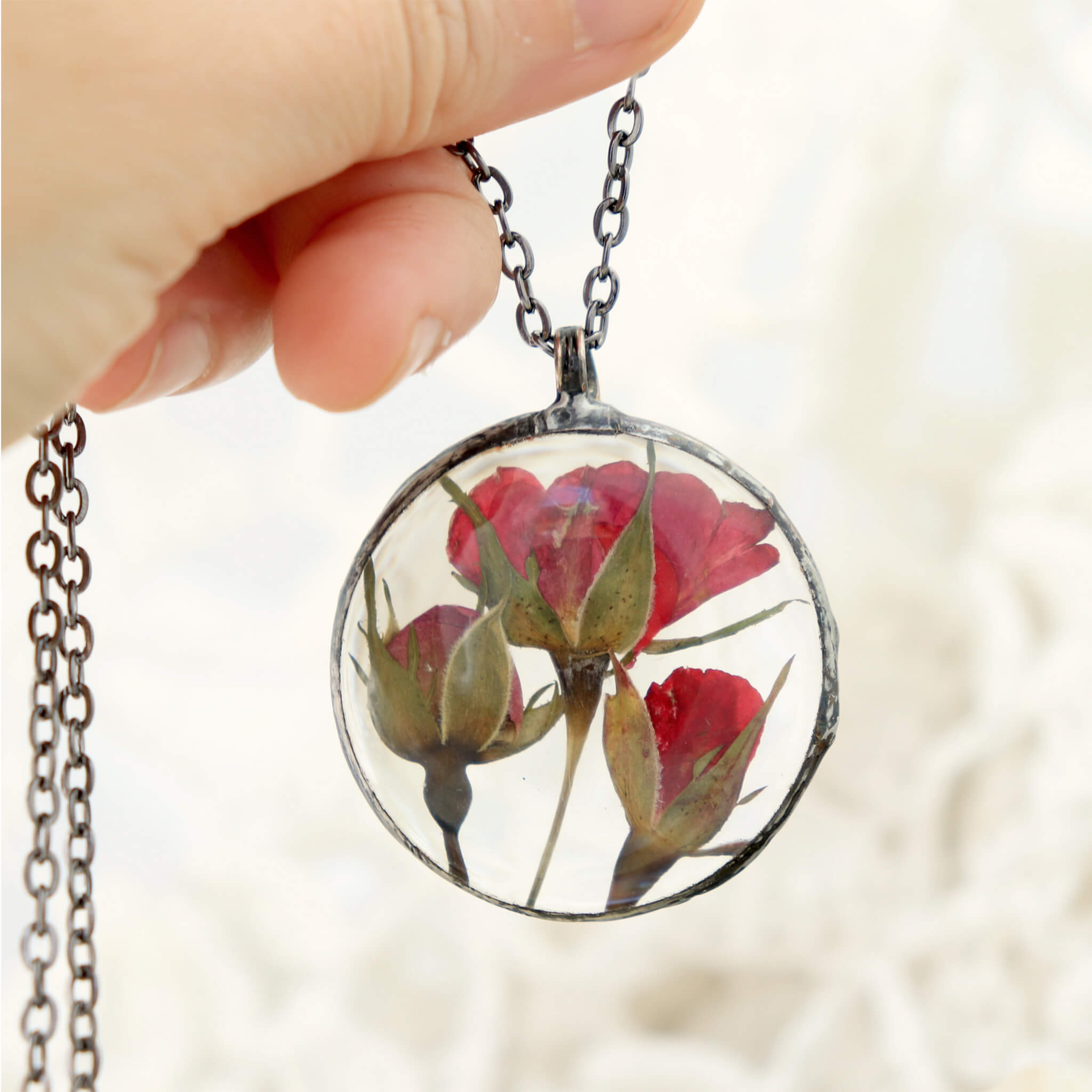 hand clutching a chain of a pressed rose pendant necklace