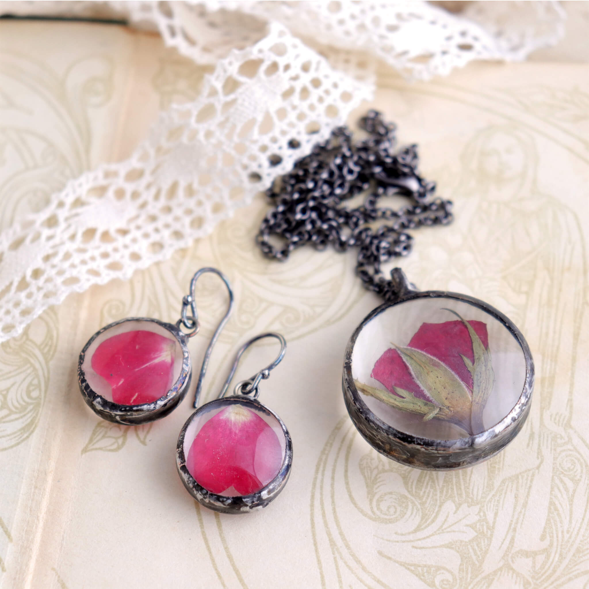 Pressed rose in soldered glass pendant necklace and earrings lying on an old book