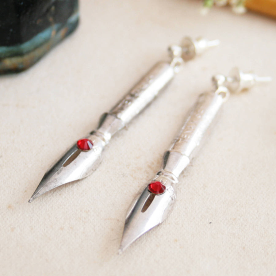 Group of pen nib earrings with birthstone crystals on them lying on vintage paper