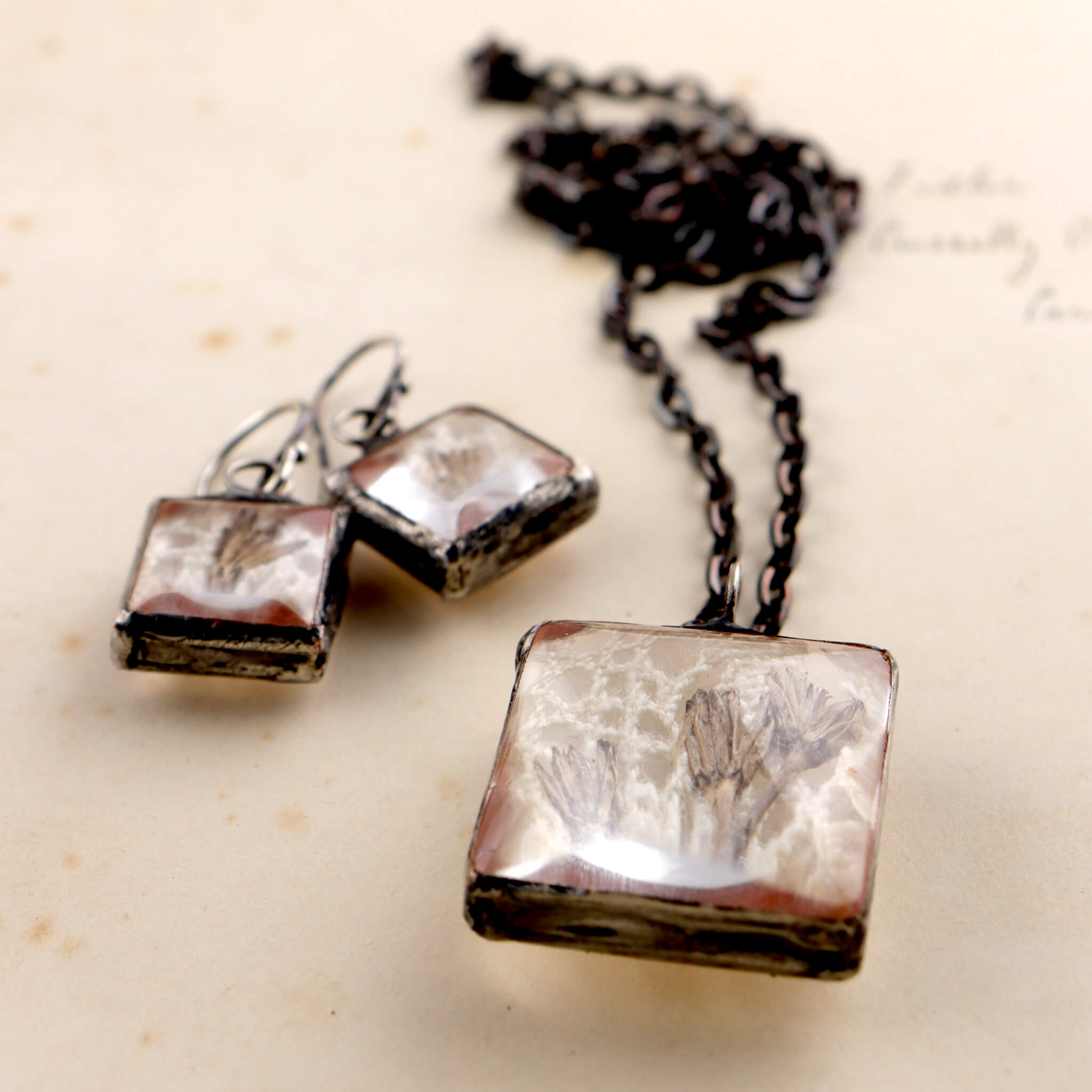 Square soldered jewellery set with vintage lase and pressed flowers lying on an old letter