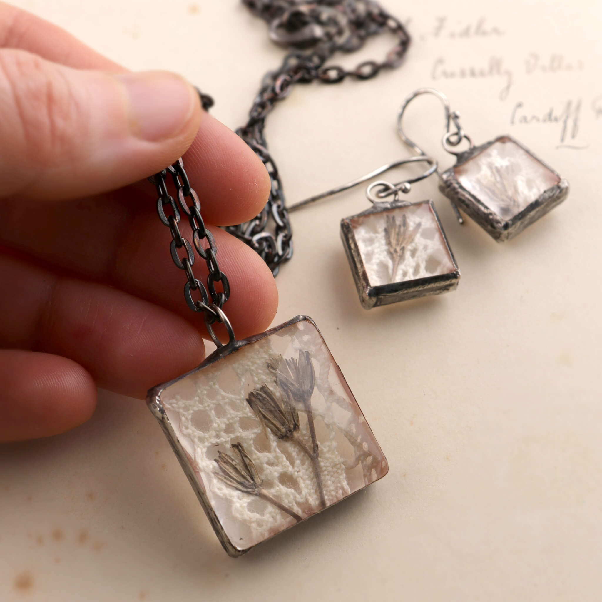 Square soldered jewellery set with vintage lase and pressed flowers hold in hand