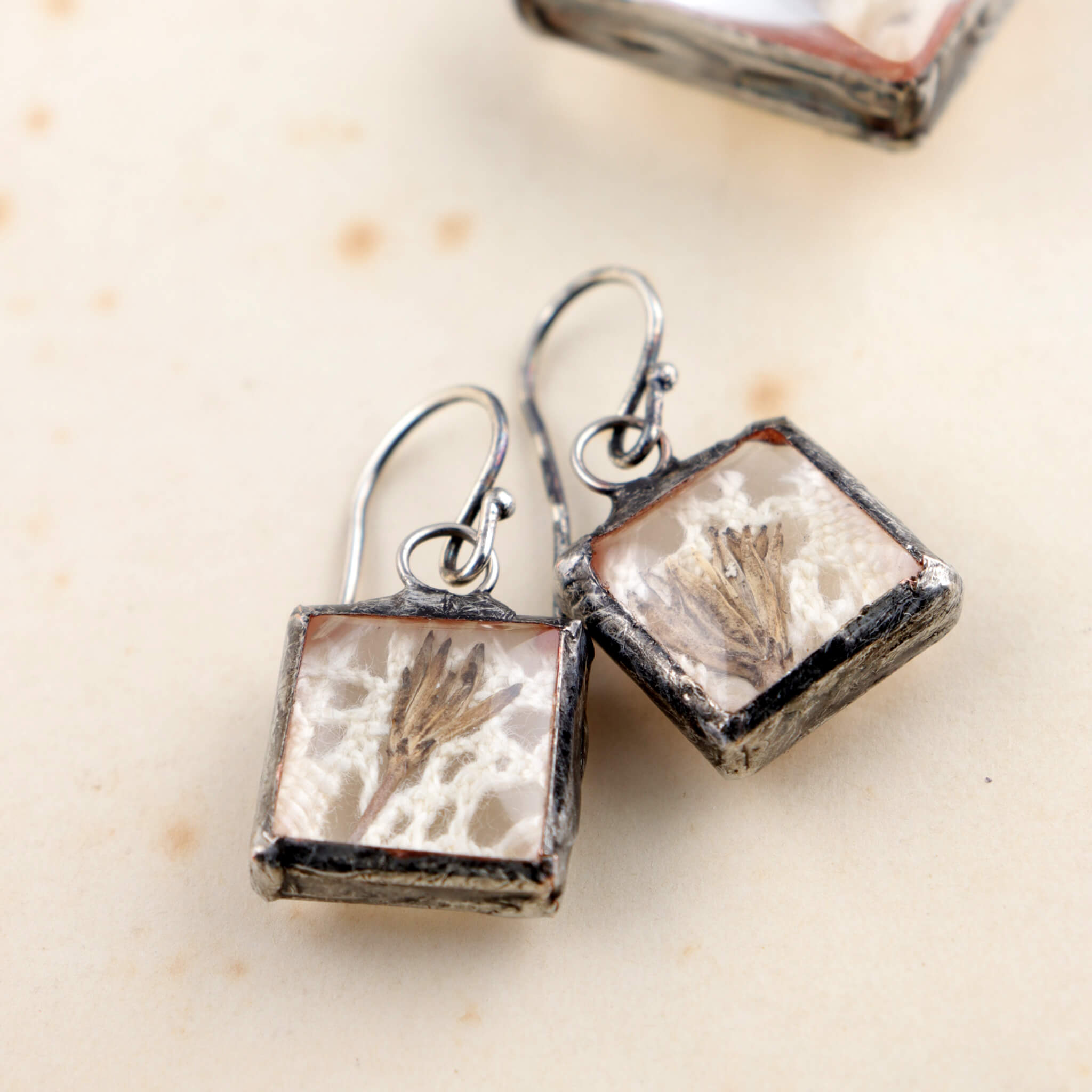 Square soldered earrings with vintage lase and pressed flowers lying on an old letter