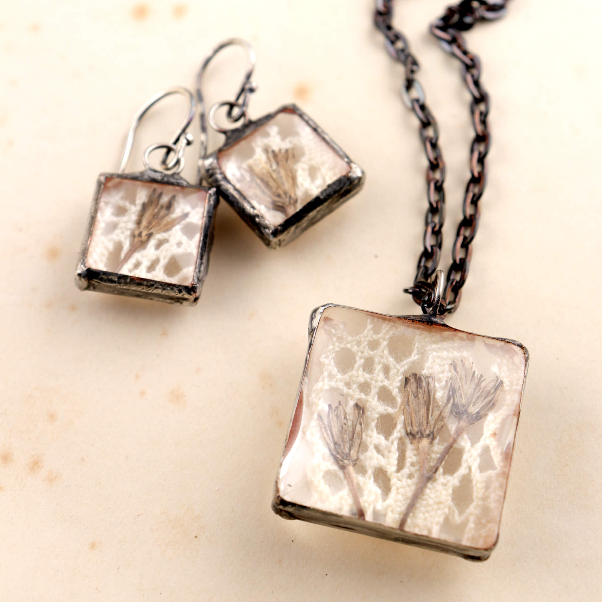 Square soldered jewellery set with vintage lase and pressed flowers lying on an old letter
