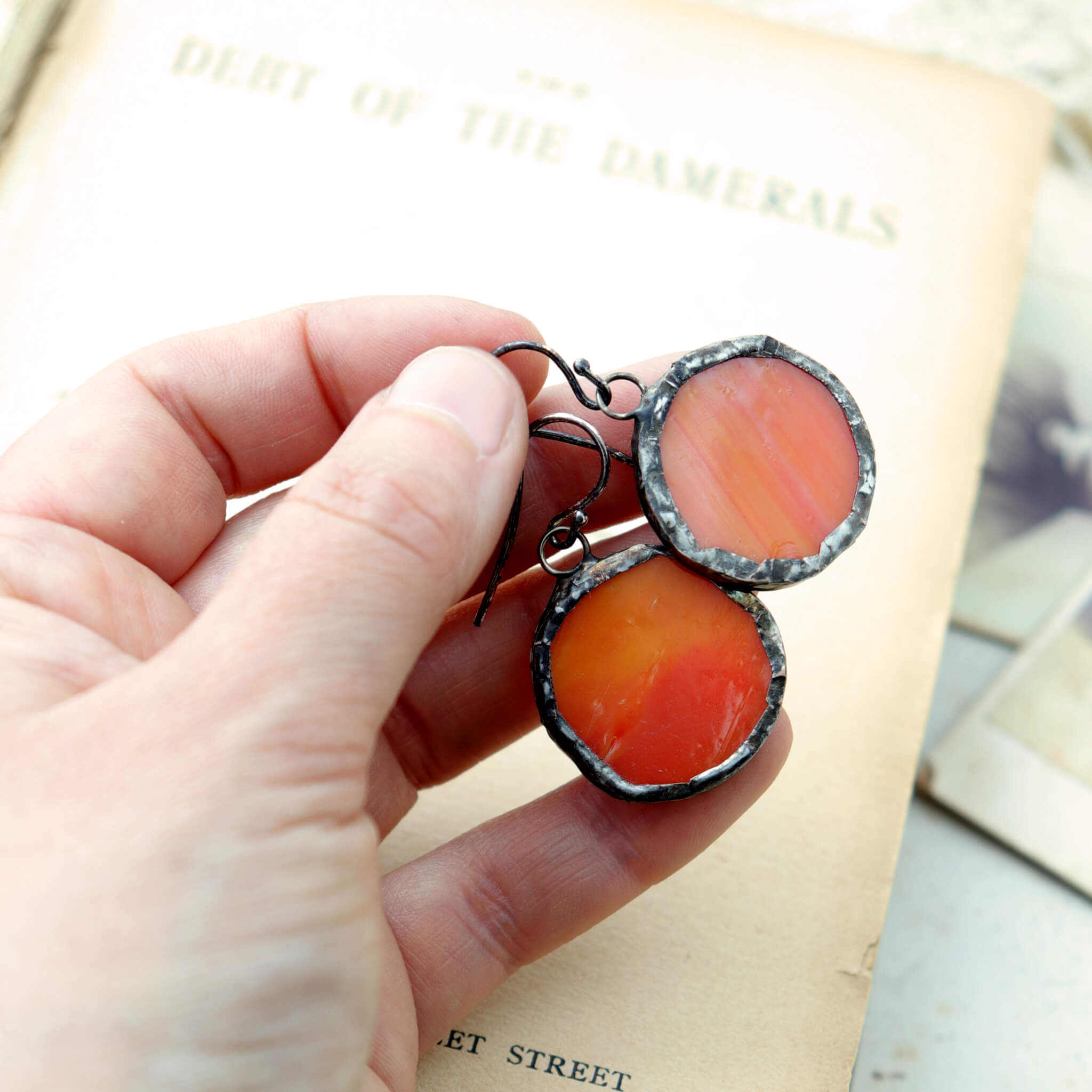 hand holding circles of glass in orange colour turned into stained glass earrings