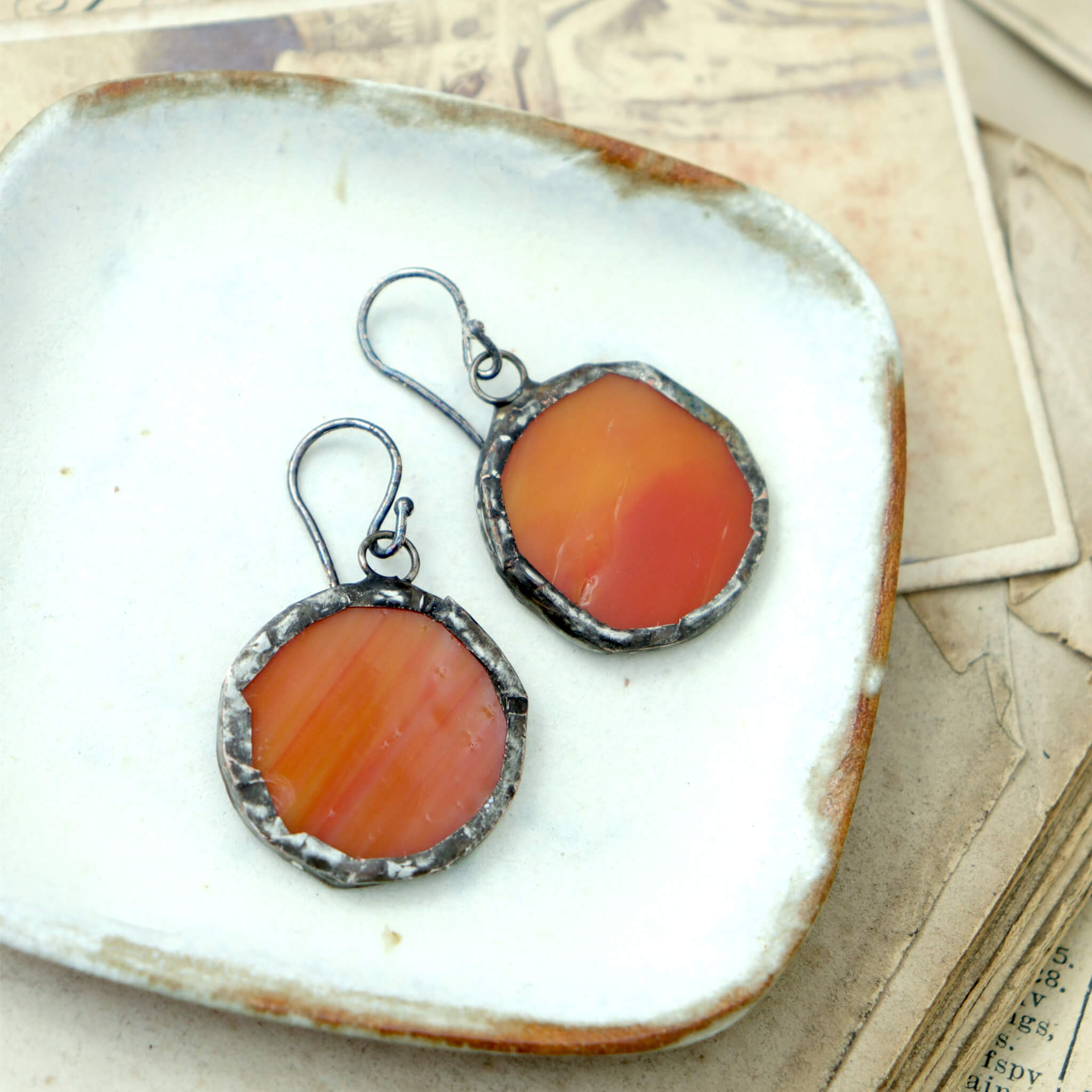 circles of glass in orange colour turned into stained glass earrings lying on a white dish