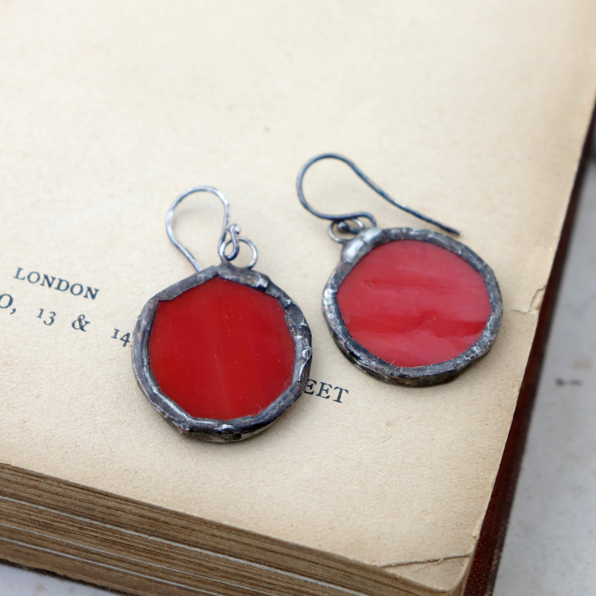 circles of glass in red colour turned into stained glass earrings lying on an open book