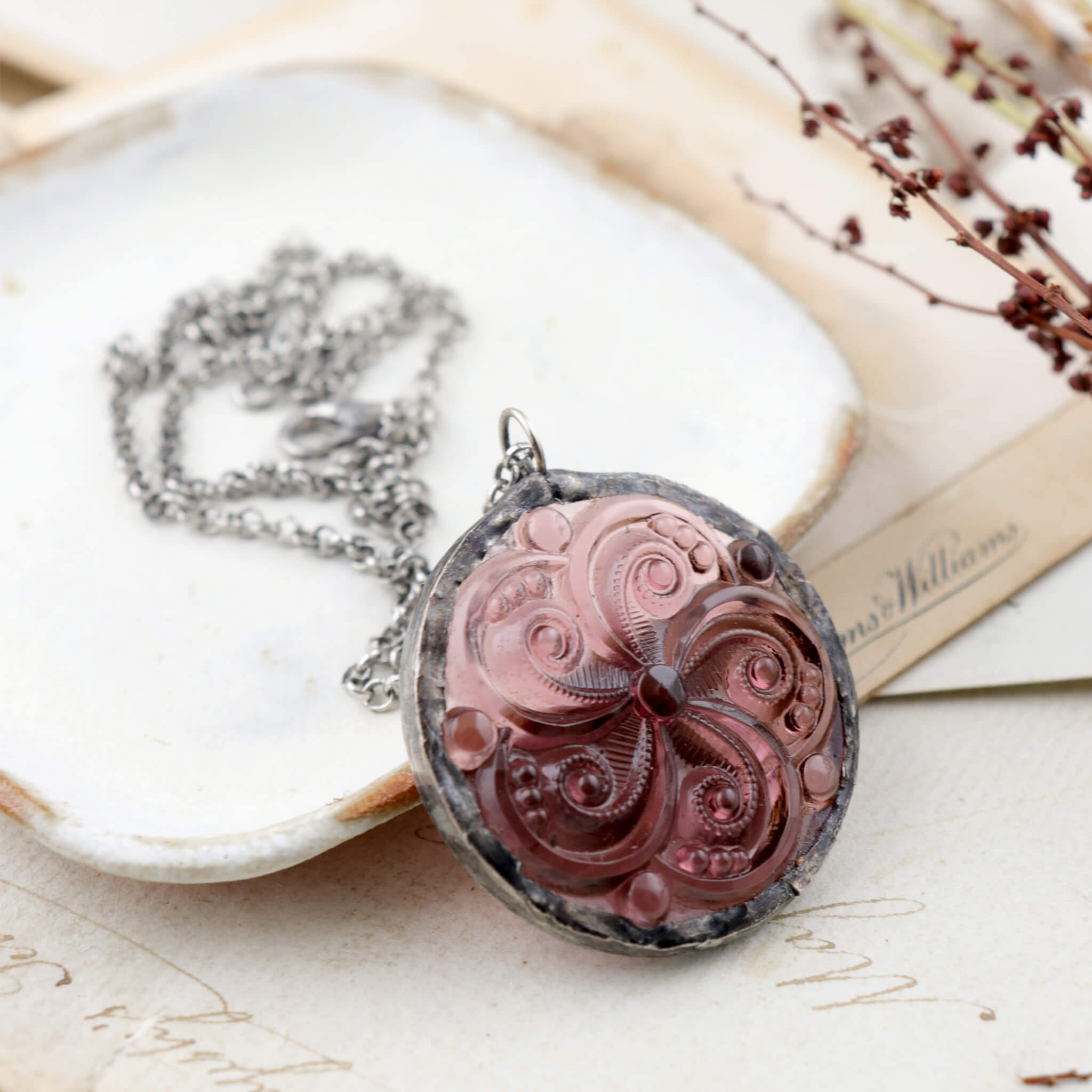 Amethyst swirl glass rondelle framed into stained glass necklace leaning on a white dish