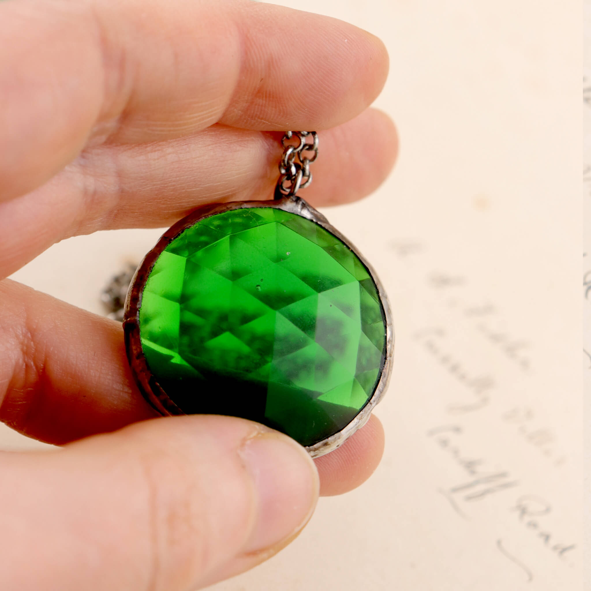 Faceted emerald glass framed into necklace hold in hand