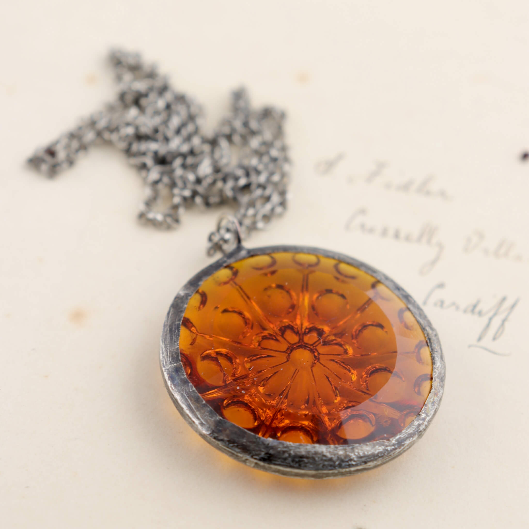Centric pattern amber glass rondelle framed into stained glass necklace lying on an old letter