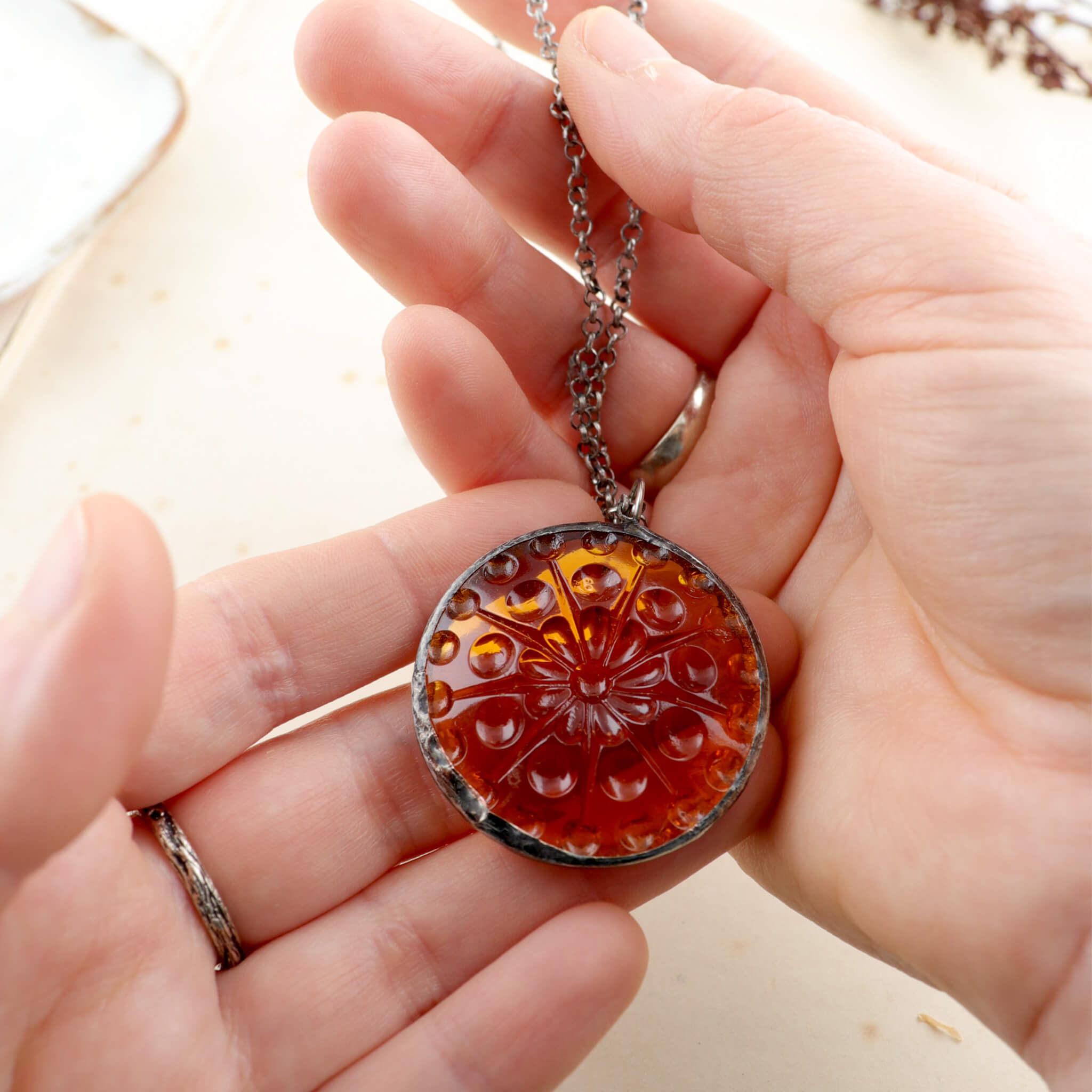 Centric pattern amber glass rondelle framed into stained glass necklace being hold in hands