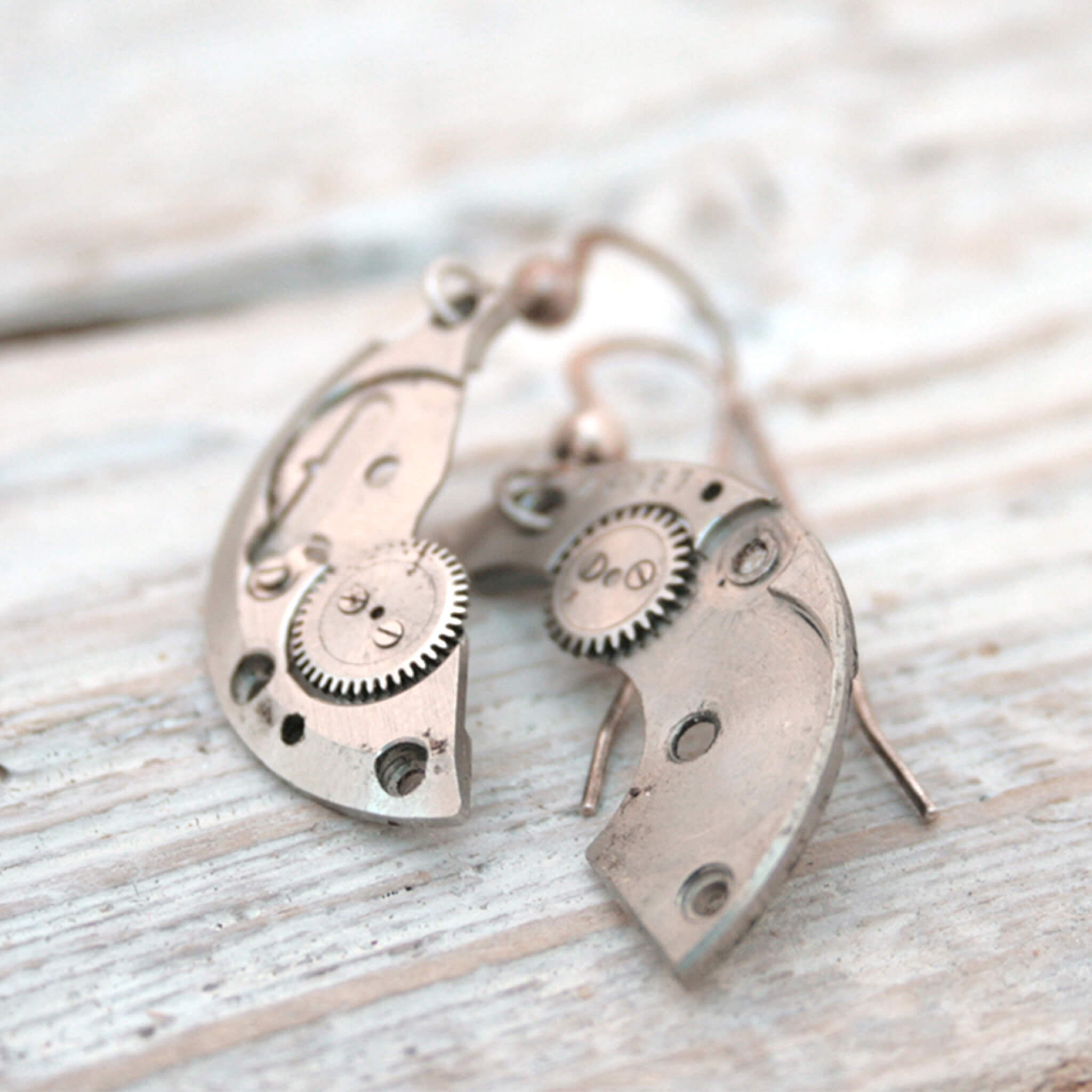 watch parts turned into dangling earrings lying on a wood painted white