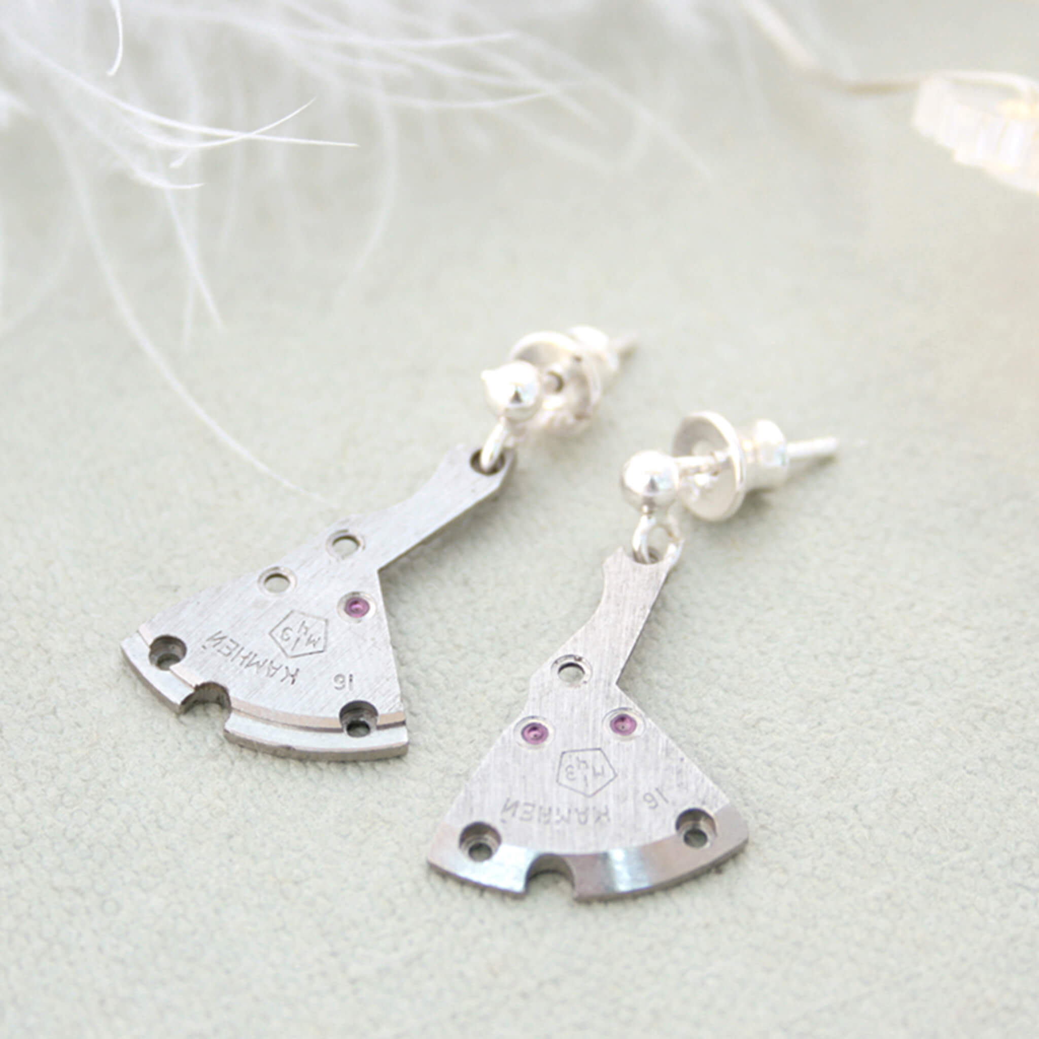 watch parts turned into dangling earrings lying on a duck egg coloured surface