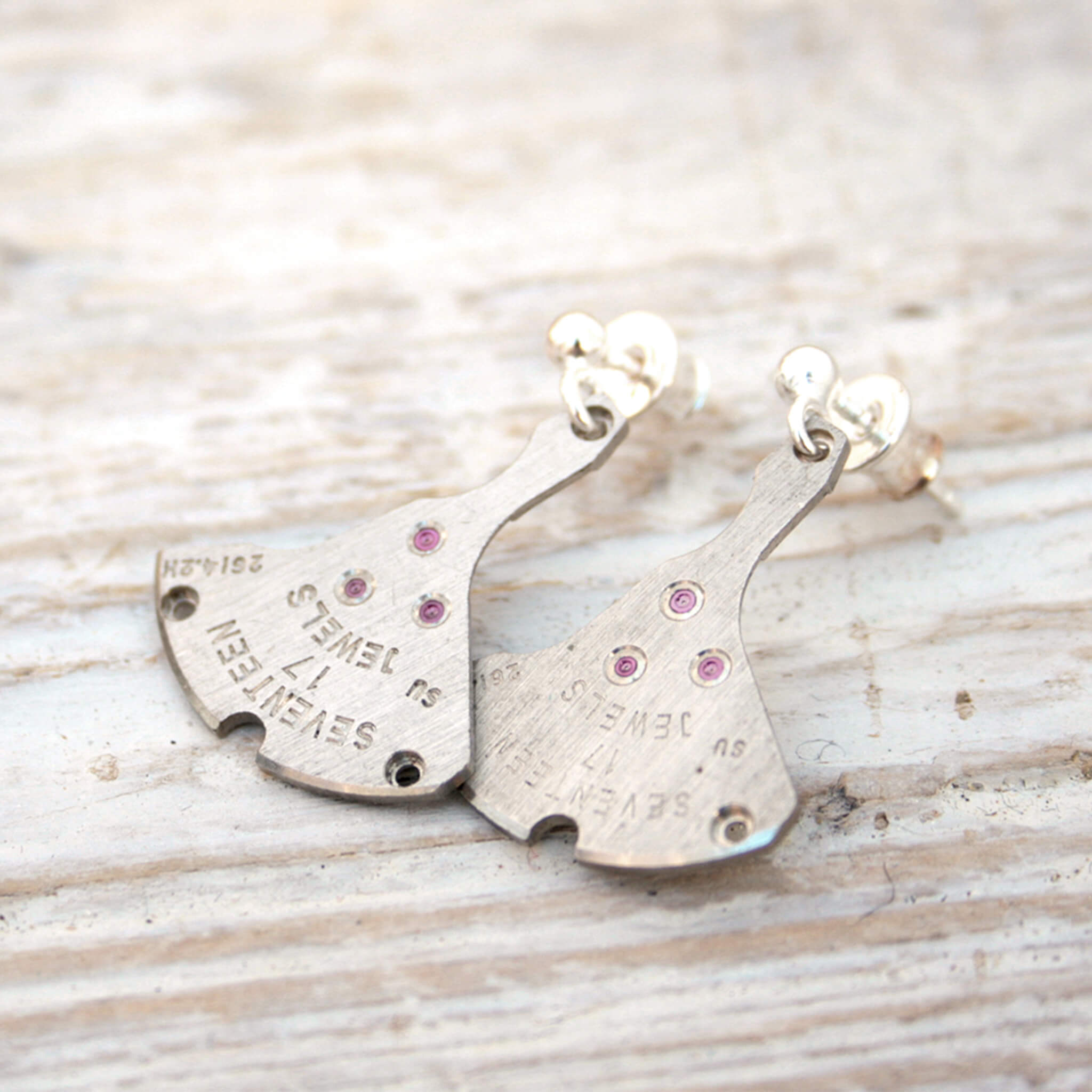 watch parts turned into dangling earrings lying on a wood painted white