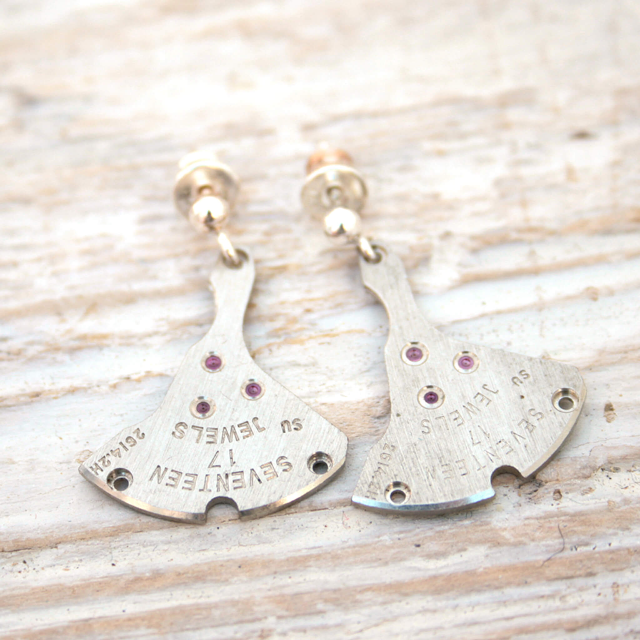watch parts turned into dangling earrings lying on a wood painted white