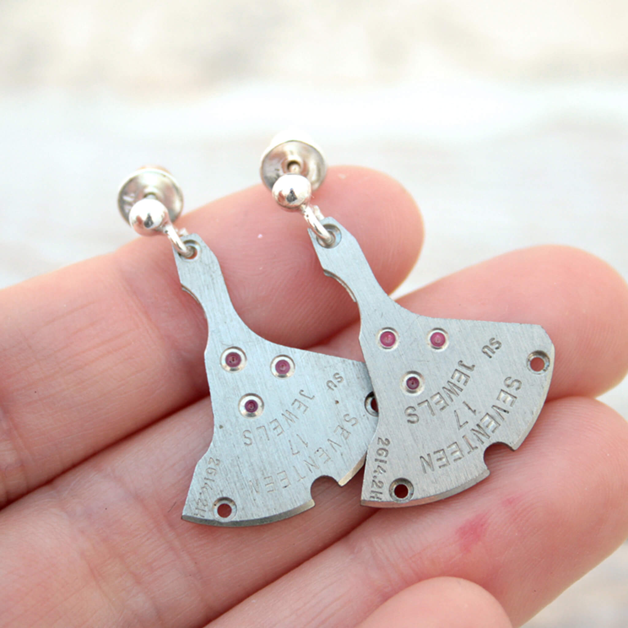 watch parts turned into dangling earrings lying on a hand