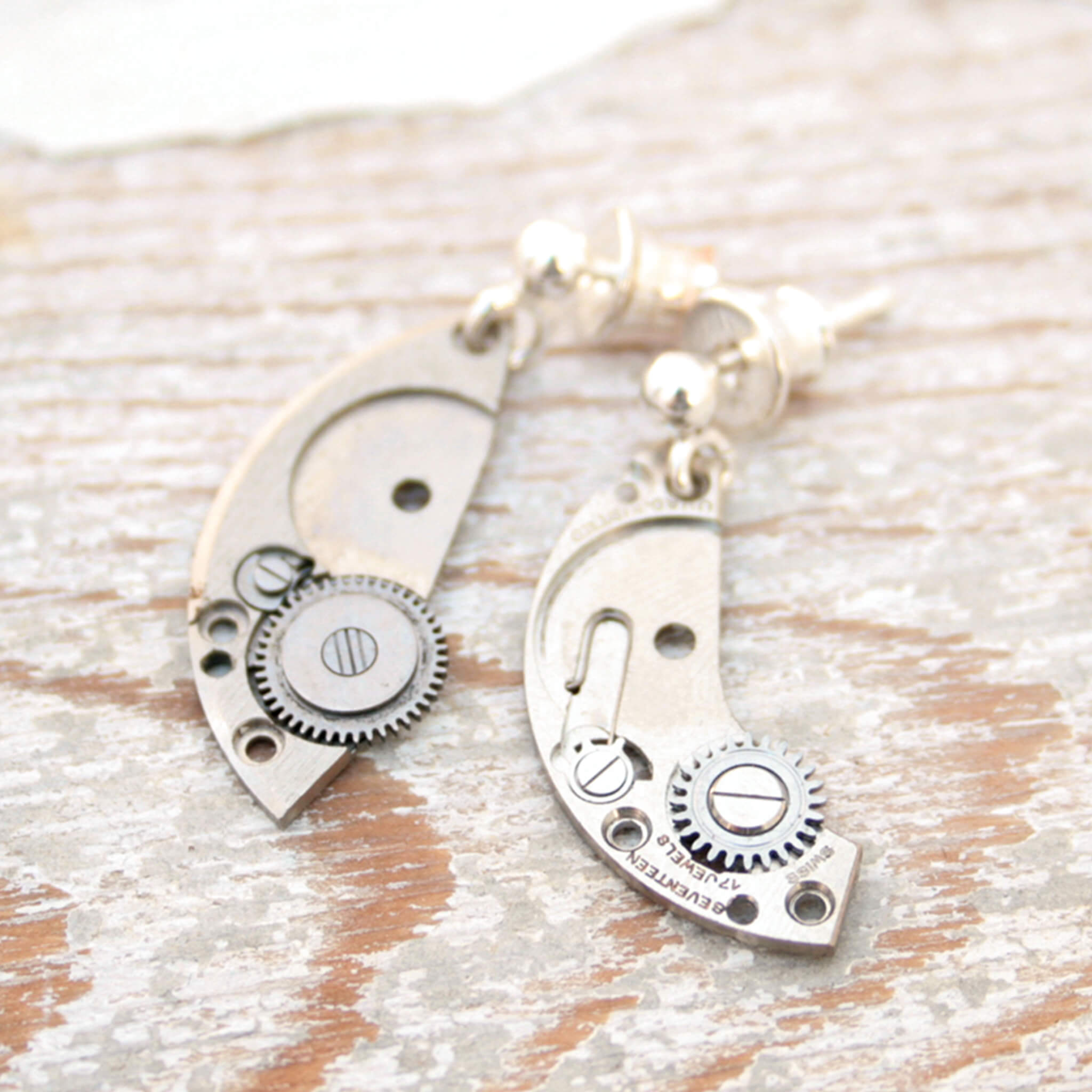 watch parts turned into dangling earrings lying on a wood painted white