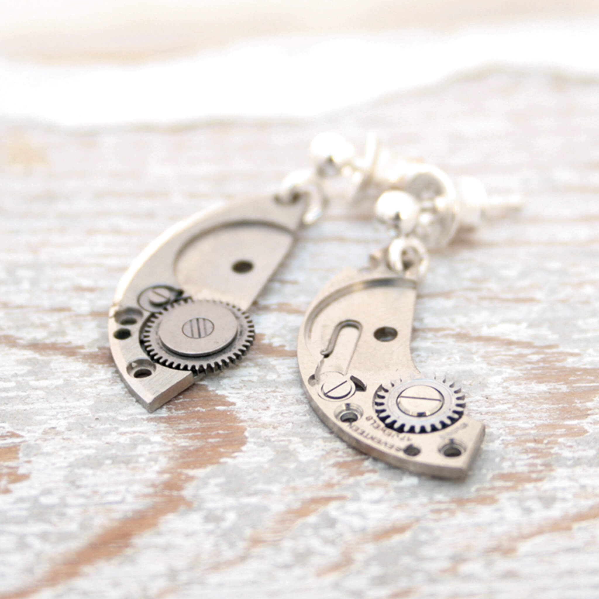 watch parts turned into dangling earrings lying on a wood painted white