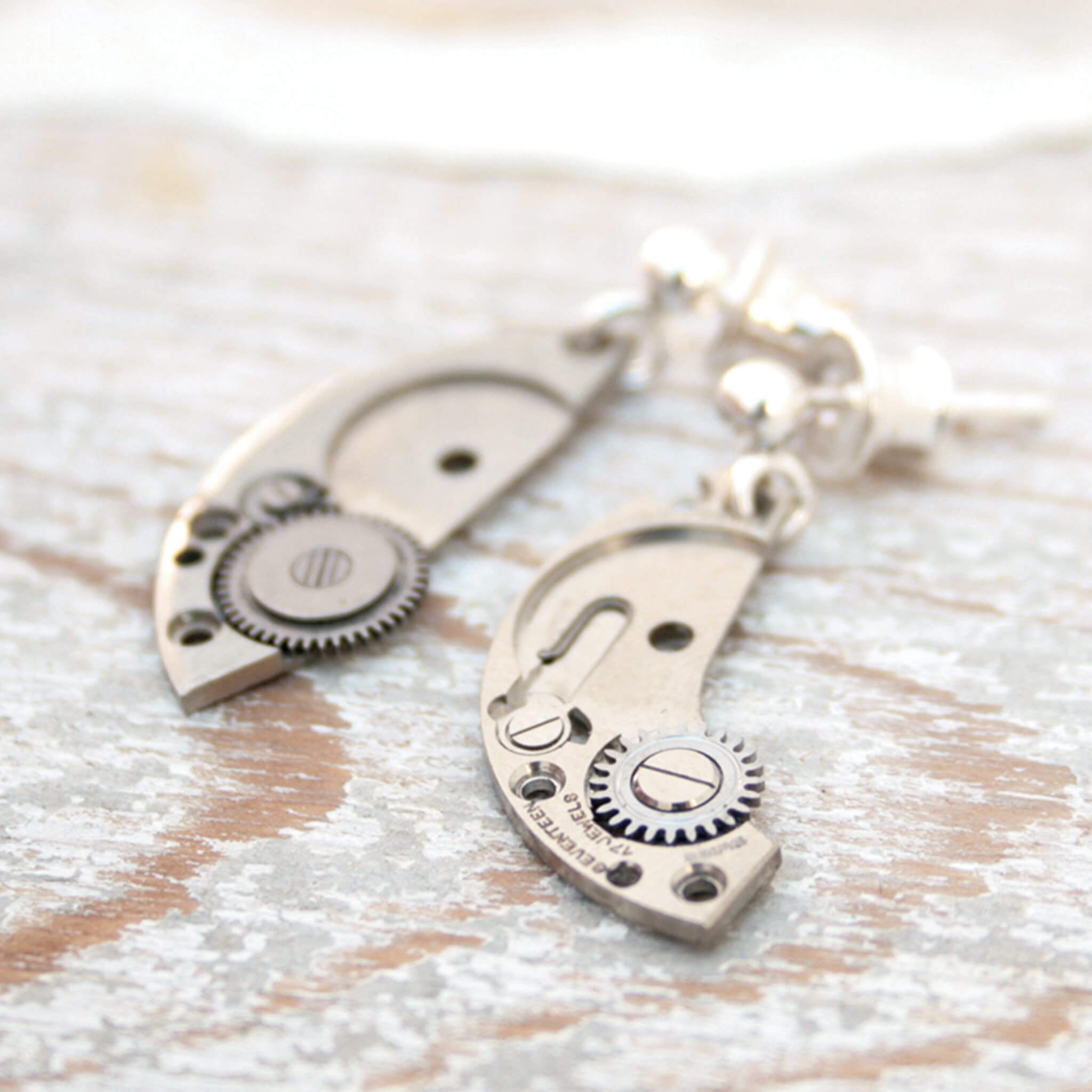 watch parts turned into dangling earrings lying on a wood painted white