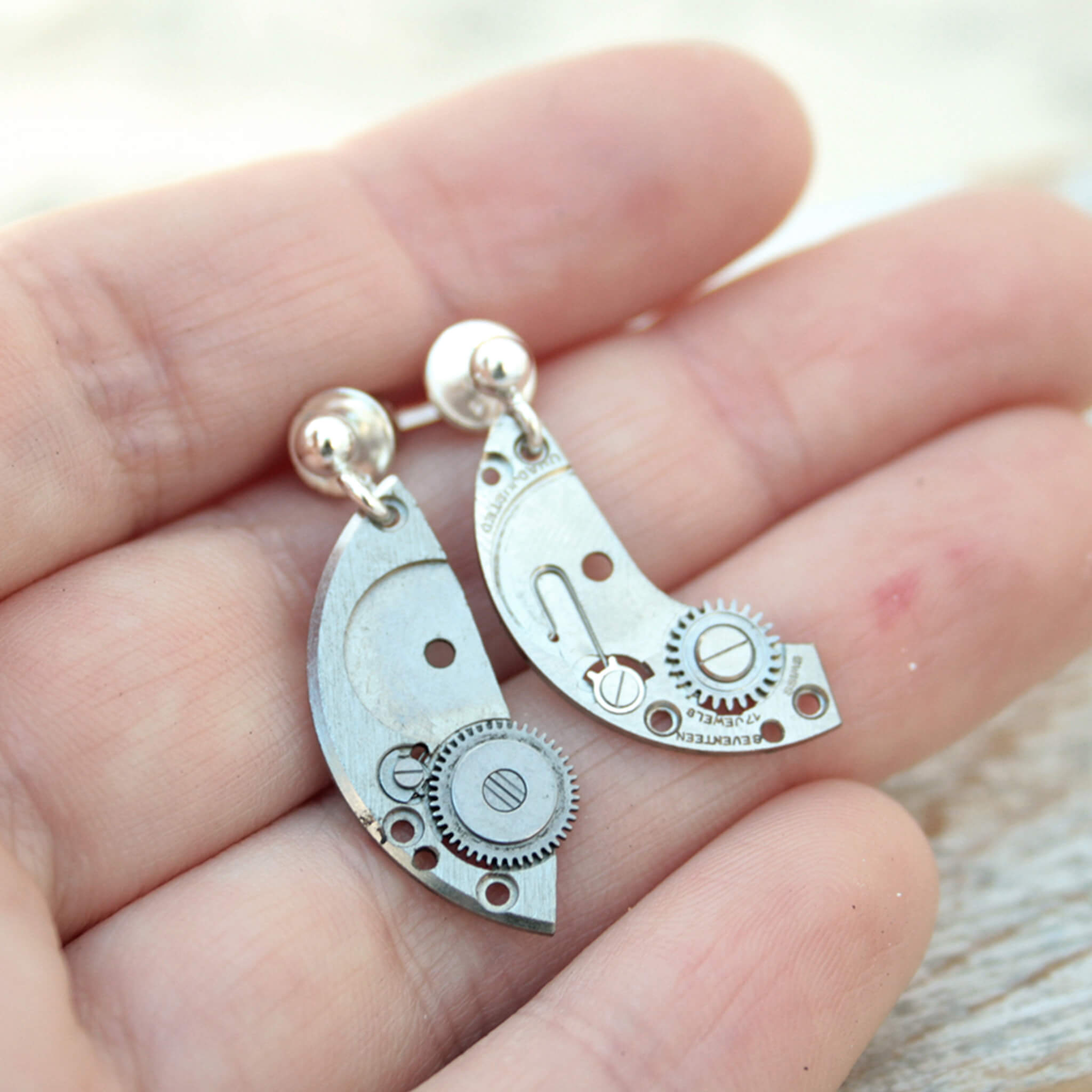 watch parts turned into dangling earrings lying on a hand