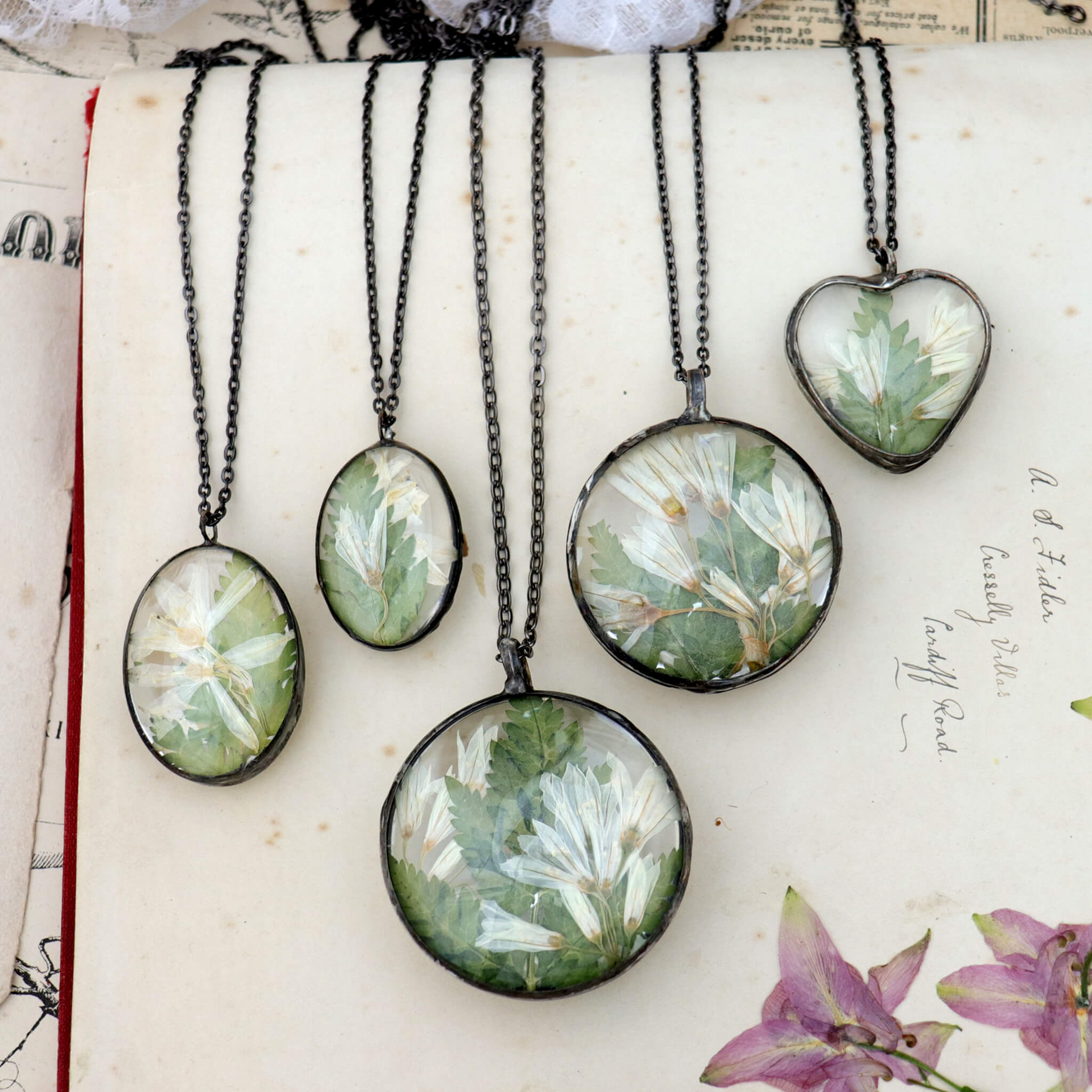 Five pressed flowers necklaces lying side by side on an old book